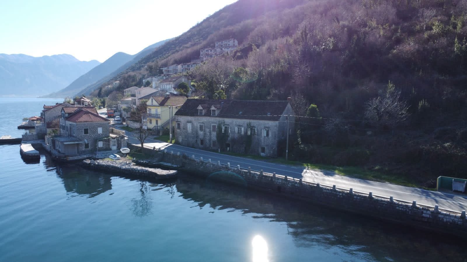 Steinhaus in erster Meereslinie in Kostanjica, Montenegro: Blick auf ein historisches Gebäude am Wasser und Berglandschaft.