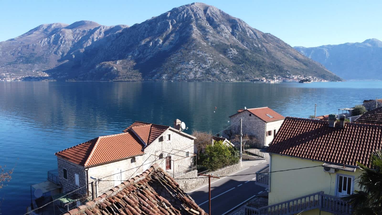 Panoramablick auf die Bucht von Kotor und die Berge vom Haus im Ort Kostanjica, Montenegro: Steingebäude mit Ziegeldächern.