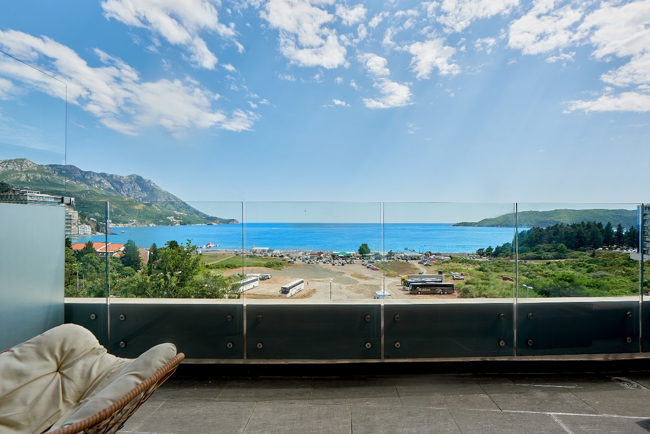 Panoramablick auf das Meer und die Berge vom geräumigen Balkon mit Glasgeländer in der Wohnung in Bečići, Montenegro.