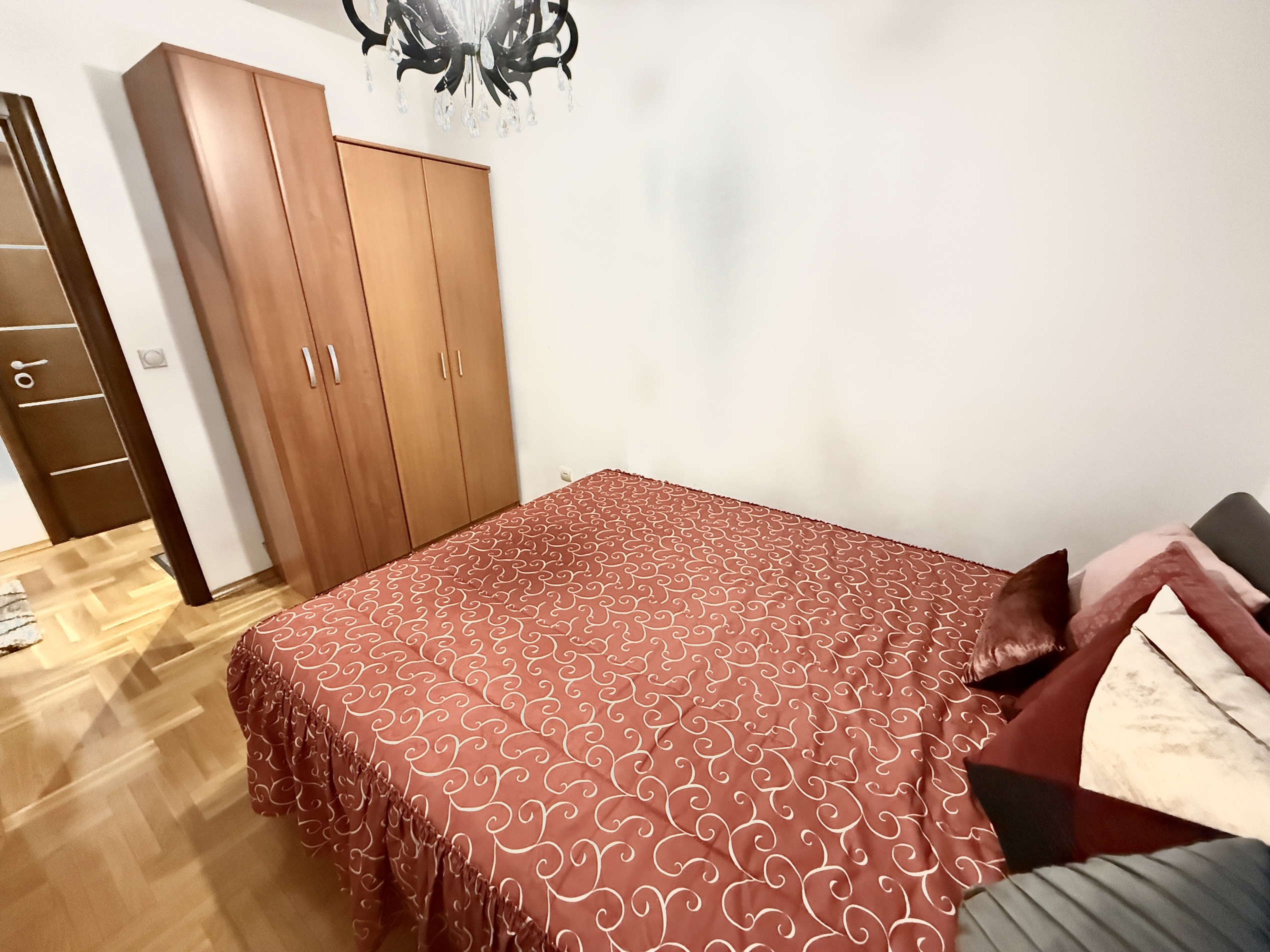 Schlafzimmer in einer Wohnung in Budva, Montenegro: Doppelbett mit roter Tagesdecke, Holzkleiderschrank und Parkettboden.
