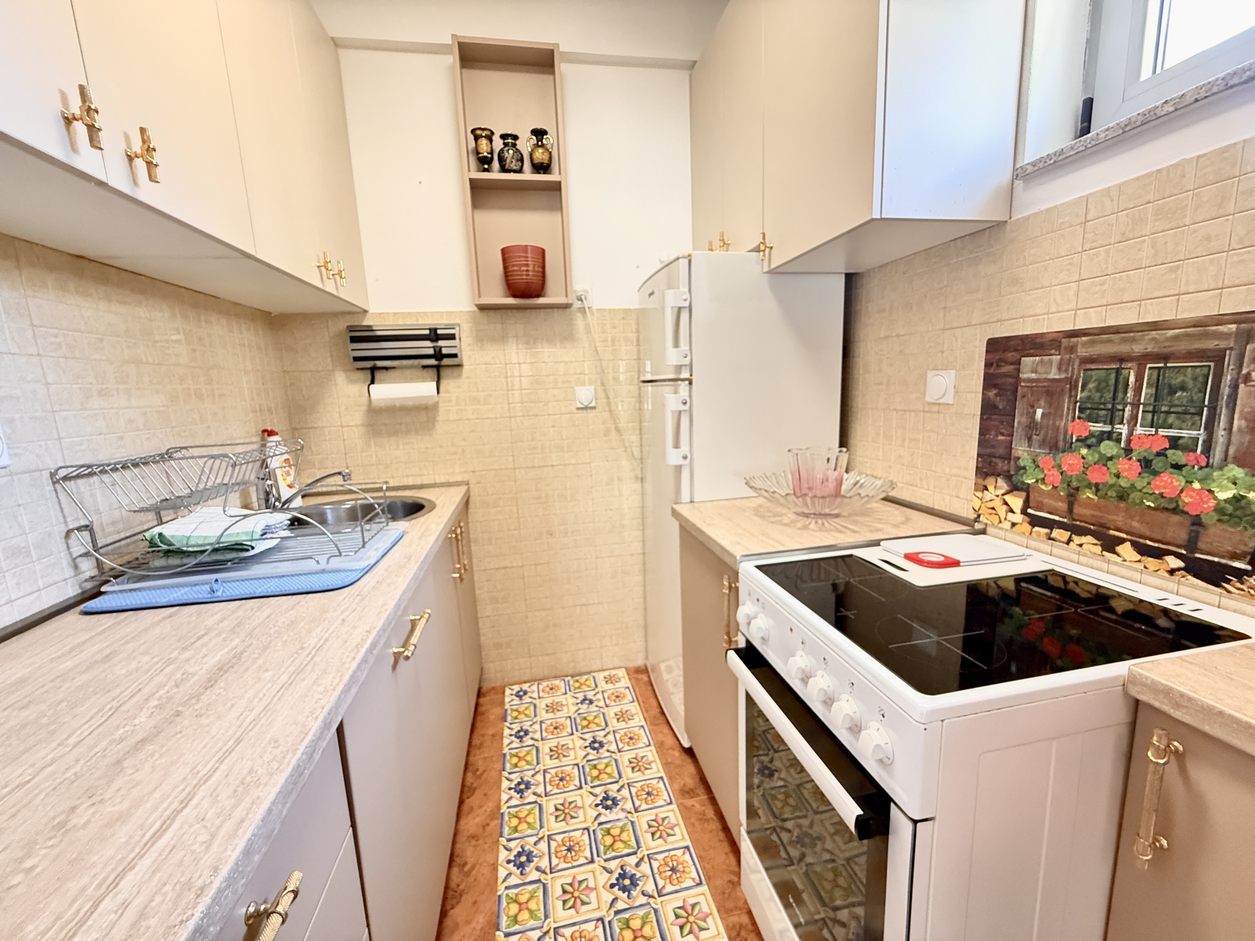 Kompakte Küche in einer Wohnung in Budva, Montenegro: helle Küchenzeile, Herd, Kühlschrank und Fliesendekor an der Wand.