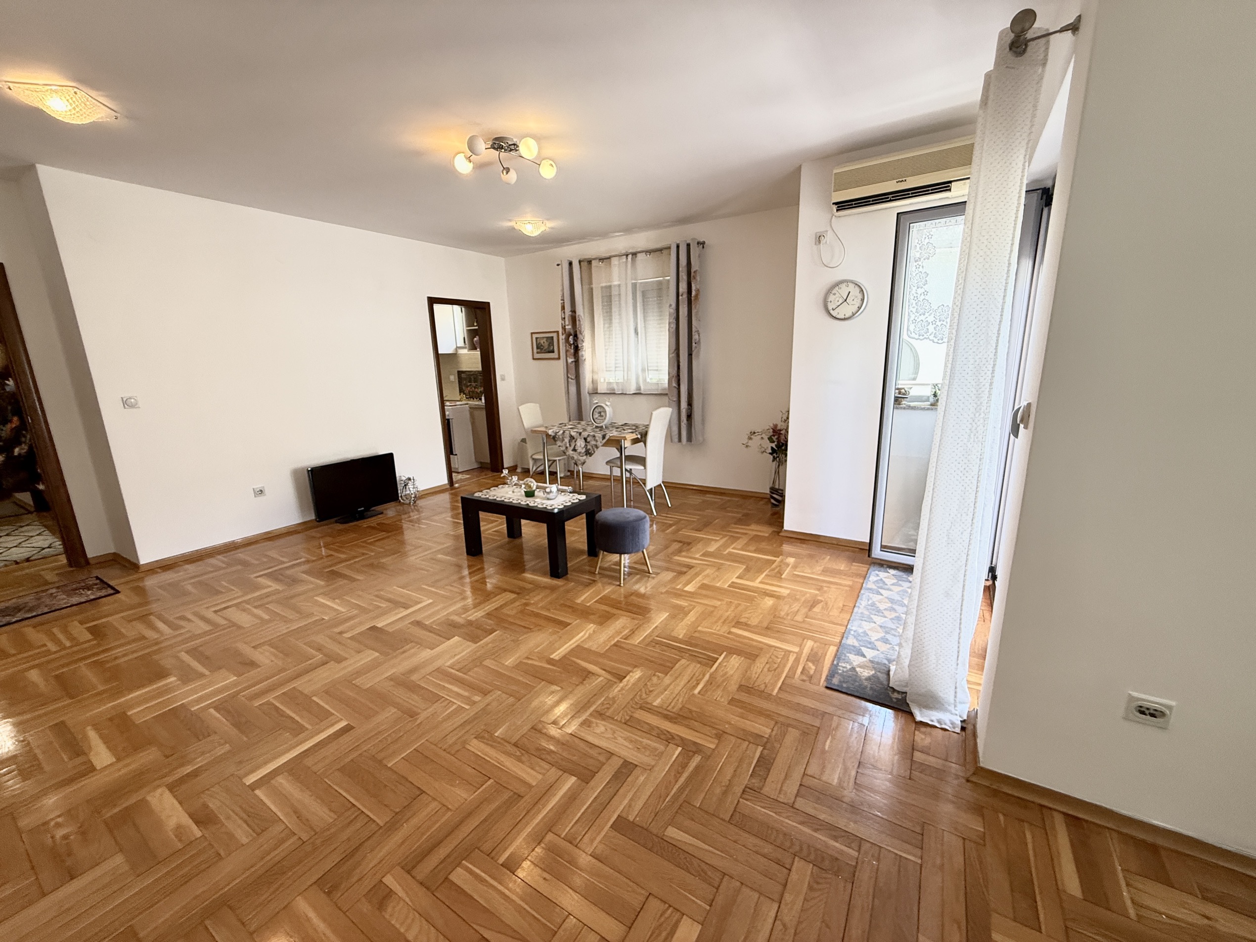 Geräumiges Wohnzimmer mit Parkett und Zugang zum Balkon in einer Wohnung, Budva, Montenegro. Möblierter Wohn- und Essbereich.