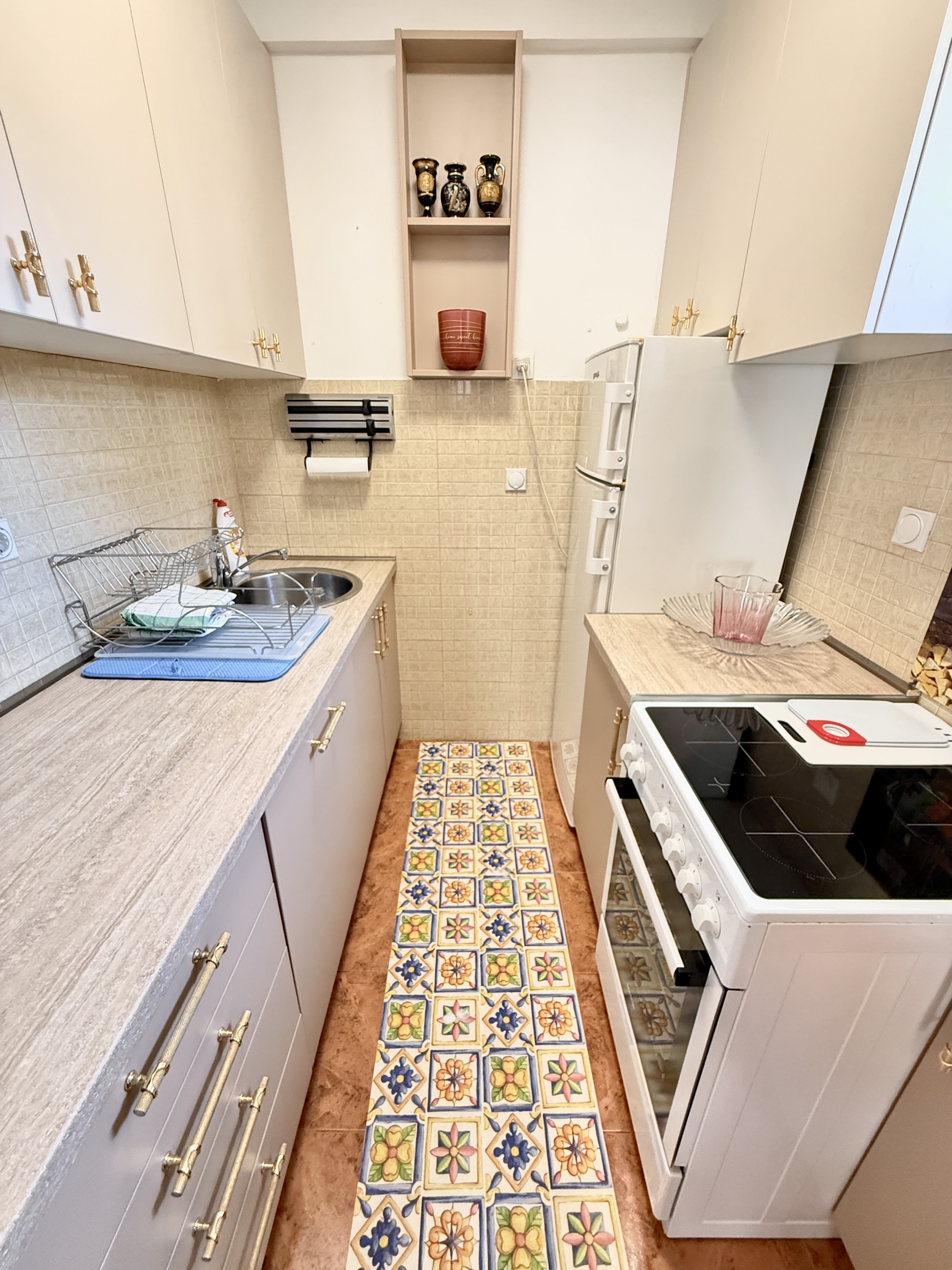 Kompakte Küche in einer Wohnung in Budva, Montenegro: helle Schränke, Herd, Spüle und auffälliges Fliesendekor auf dem Boden.