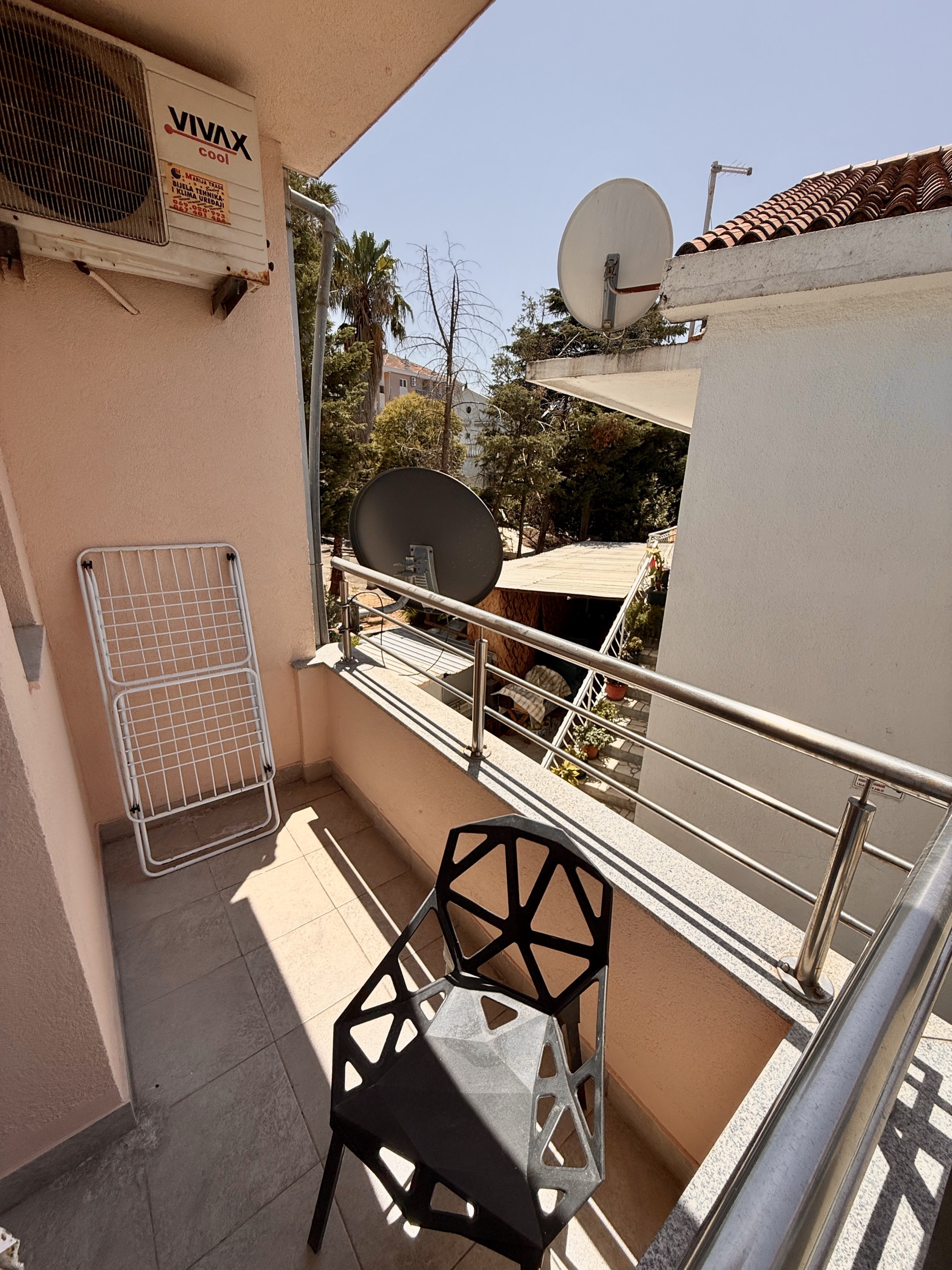 Balkon einer Wohnung in Budva, Montenegro: moderner Stuhl, Wäscheständer, Klimaanlage und Blick auf den grünen Innenhof.
