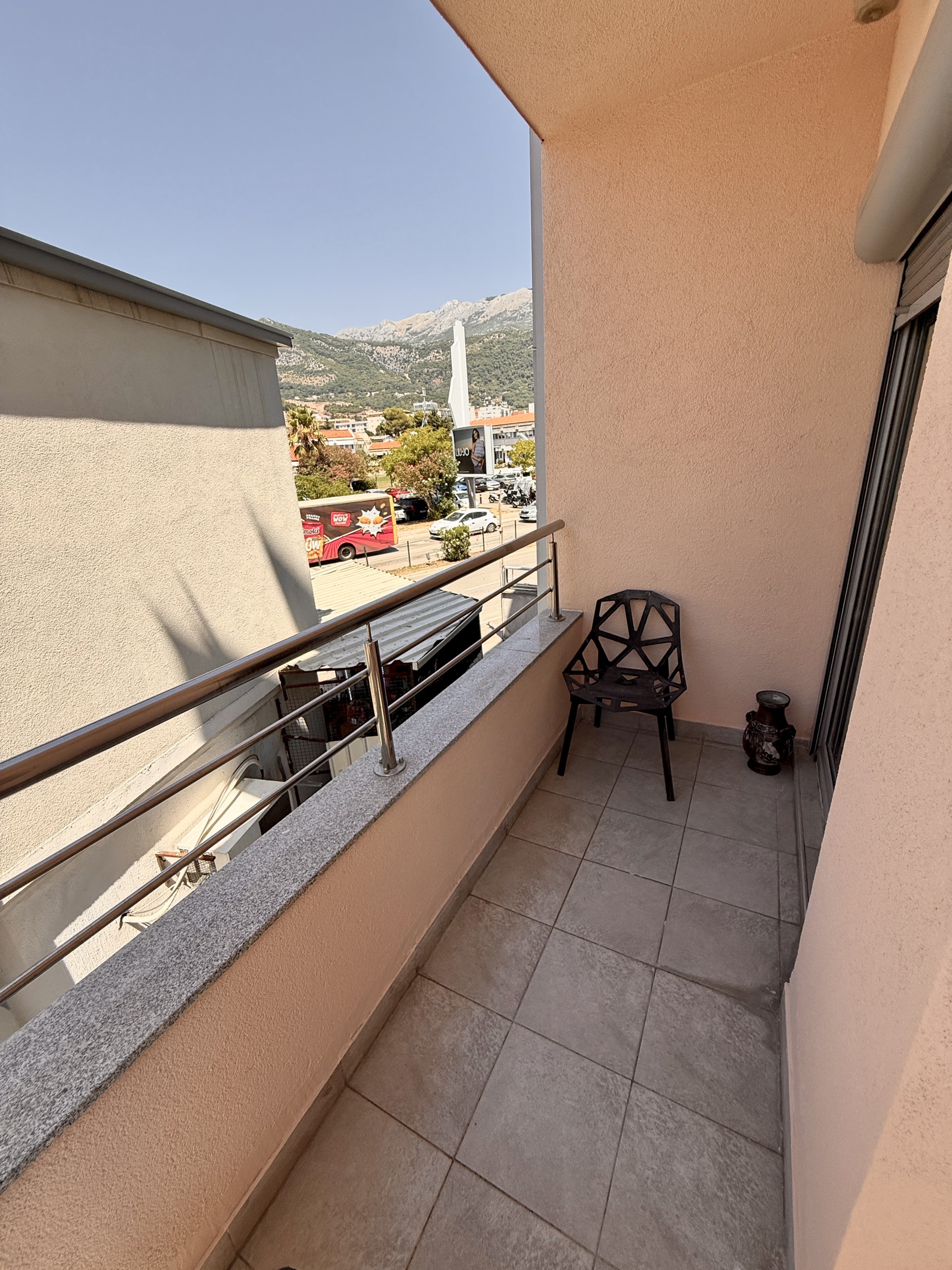 Balkon der Wohnung in Budva, Montenegro: Fliesenboden, moderner Stuhl, Blick auf die Berge und die städtische Infrastruktur.