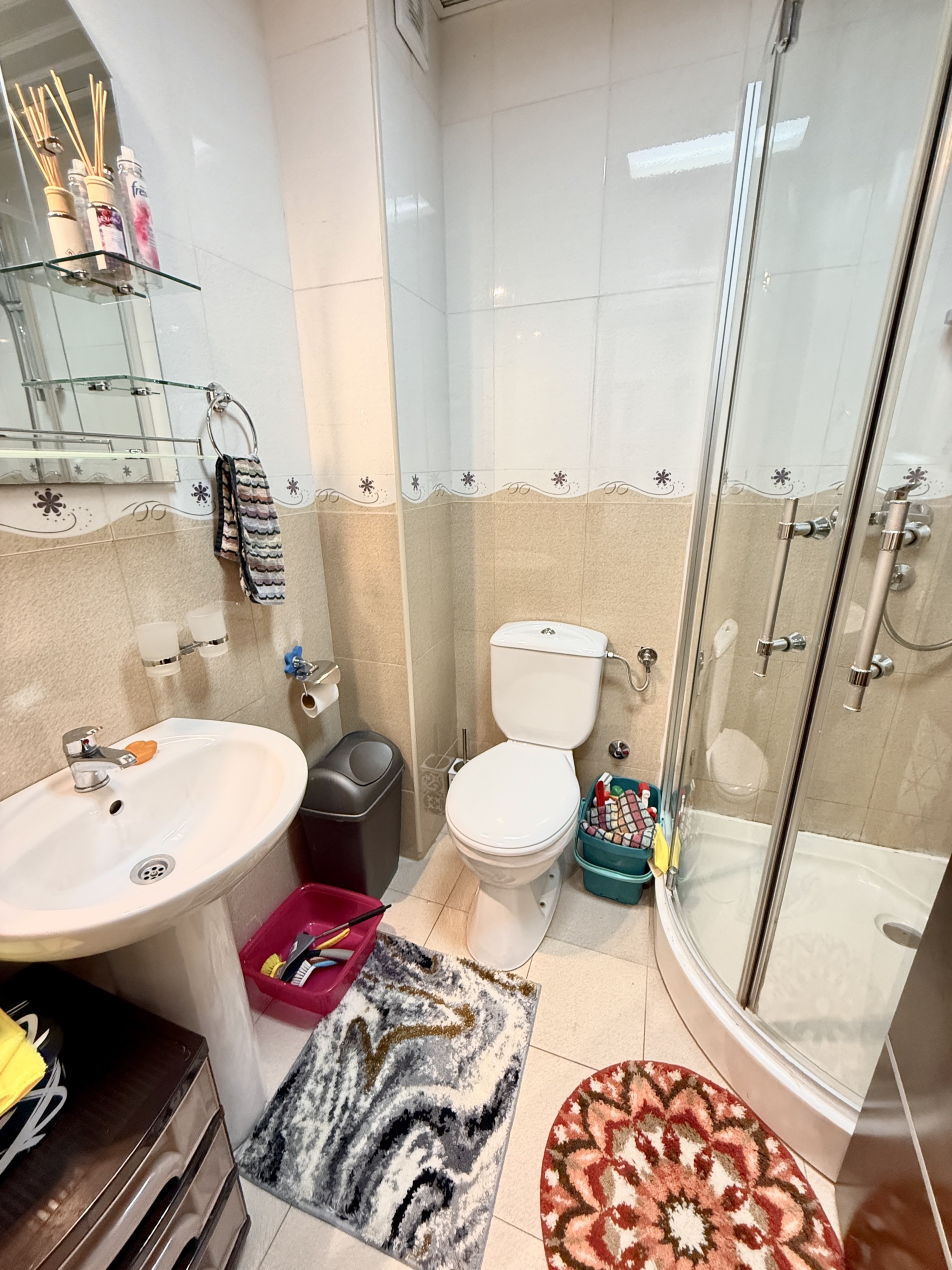 Badezimmer in einer Wohnung in Budva, Montenegro: Duschkabine, Waschbecken, Toilette und helle Fliesenverkleidung.