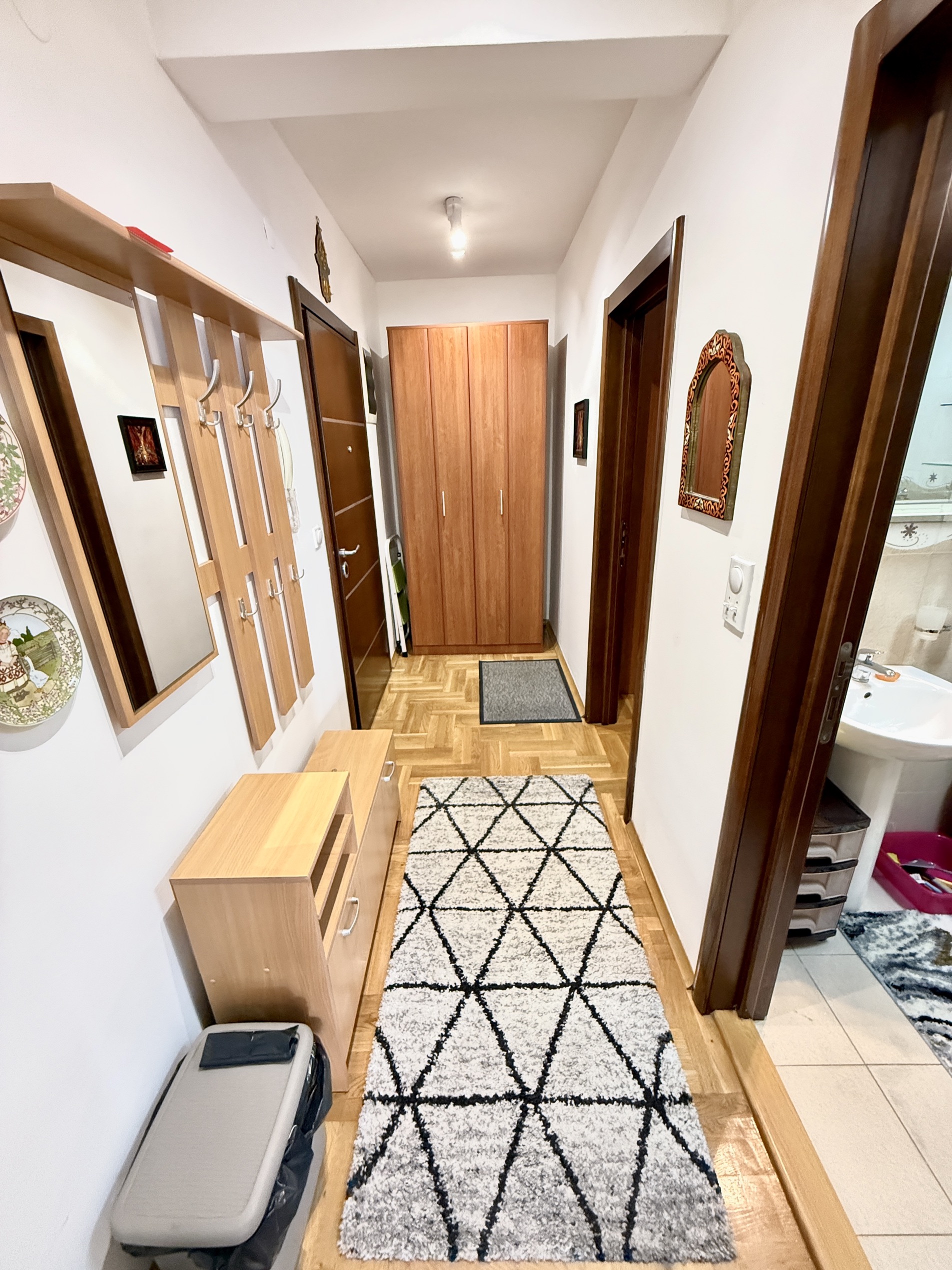 Heller Flur in einer Wohnung in Budva, Montenegro: Parkettboden, Holzschrank, Garderobe mit Spiegel und Teppich.