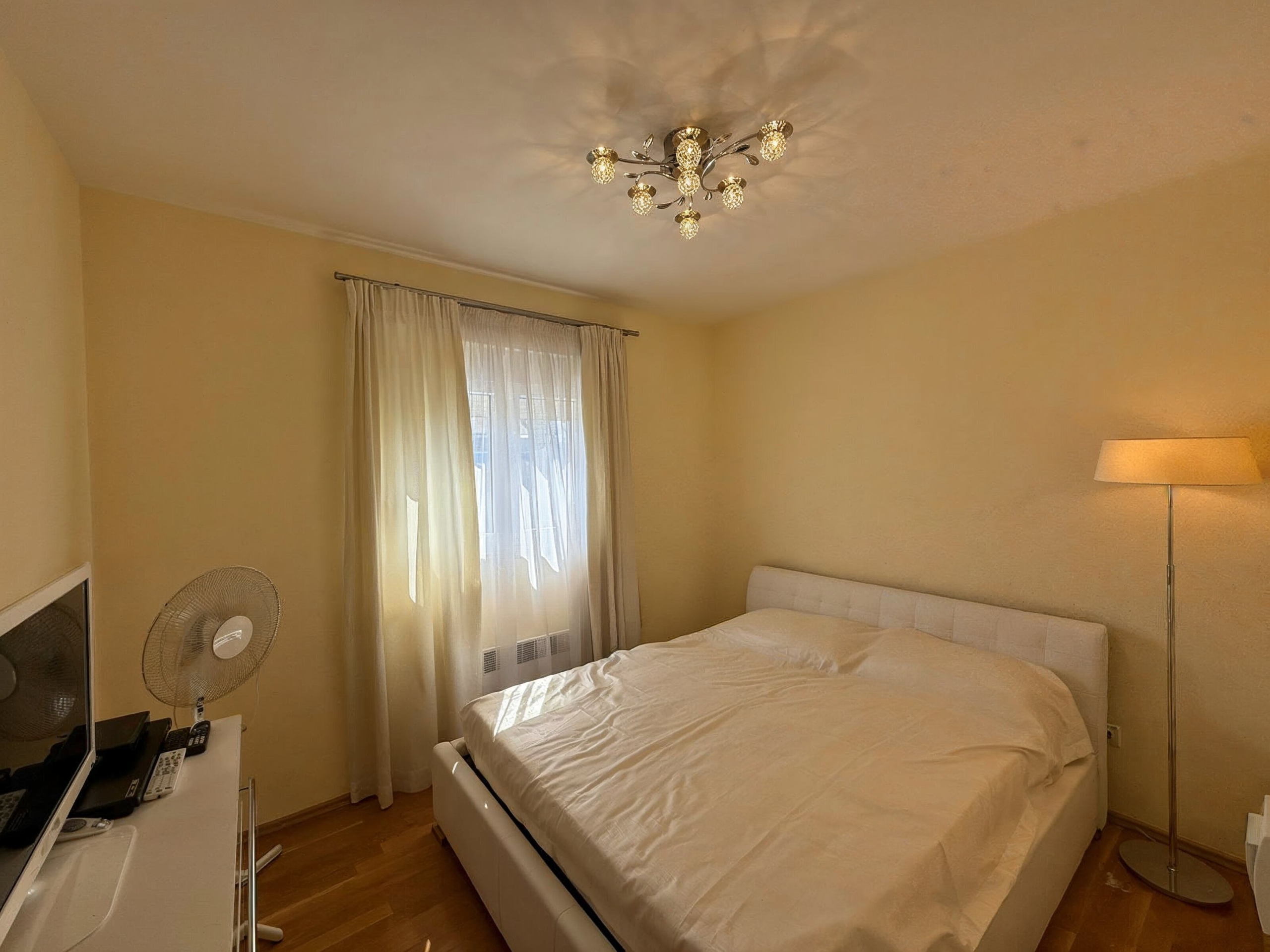 Gemütliches Schlafzimmer mit Doppelbett in einer Wohnung in Bečići, Montenegro: helles Interieur, Parkett und stilvoller Kronleuchter.