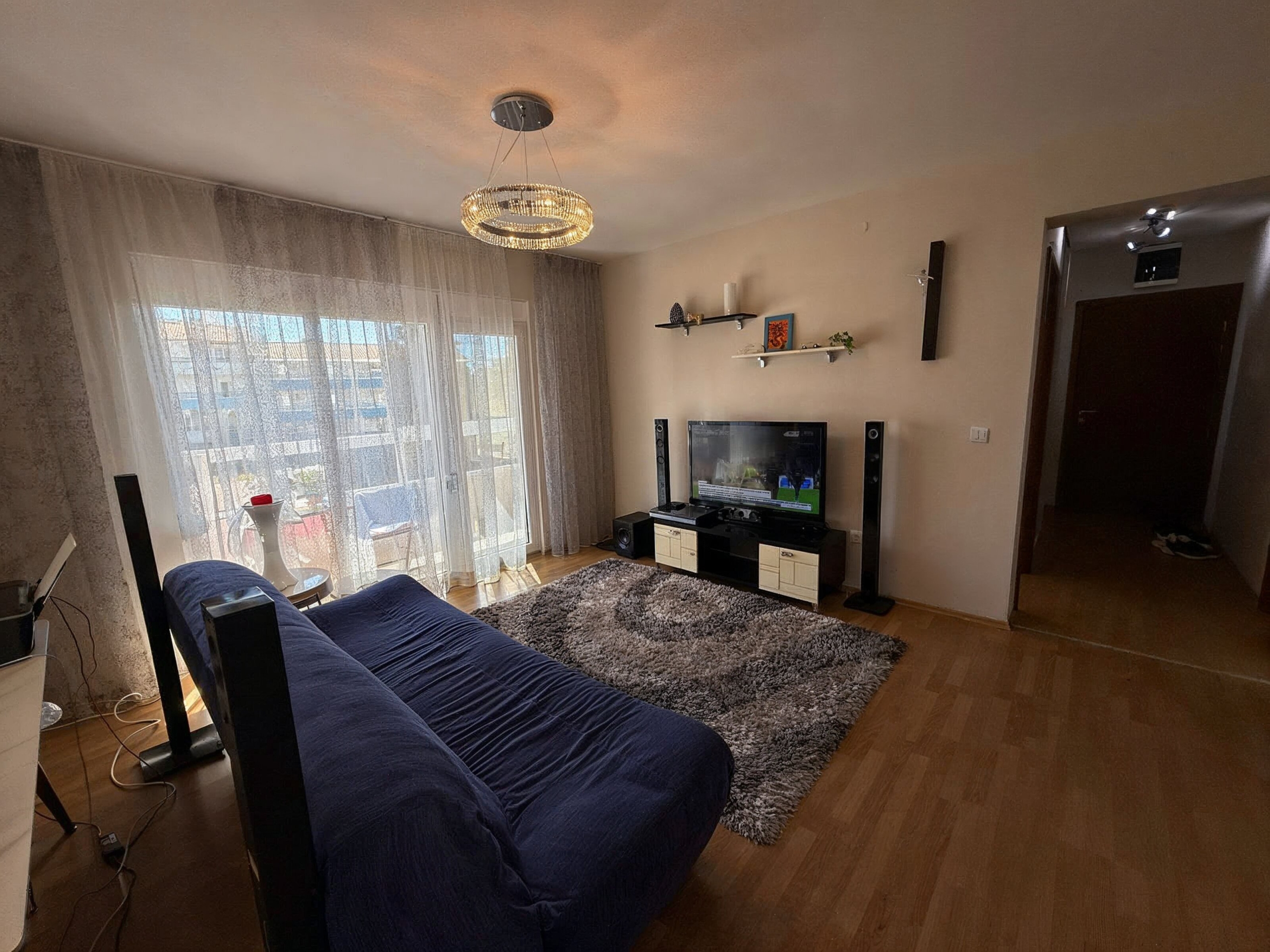 Gemütliches Wohnzimmer in einer Wohnung in Bečići, Montenegro: blaues Sofa, TV-Bereich, Panoramafenster mit Zugang zur Terrasse.