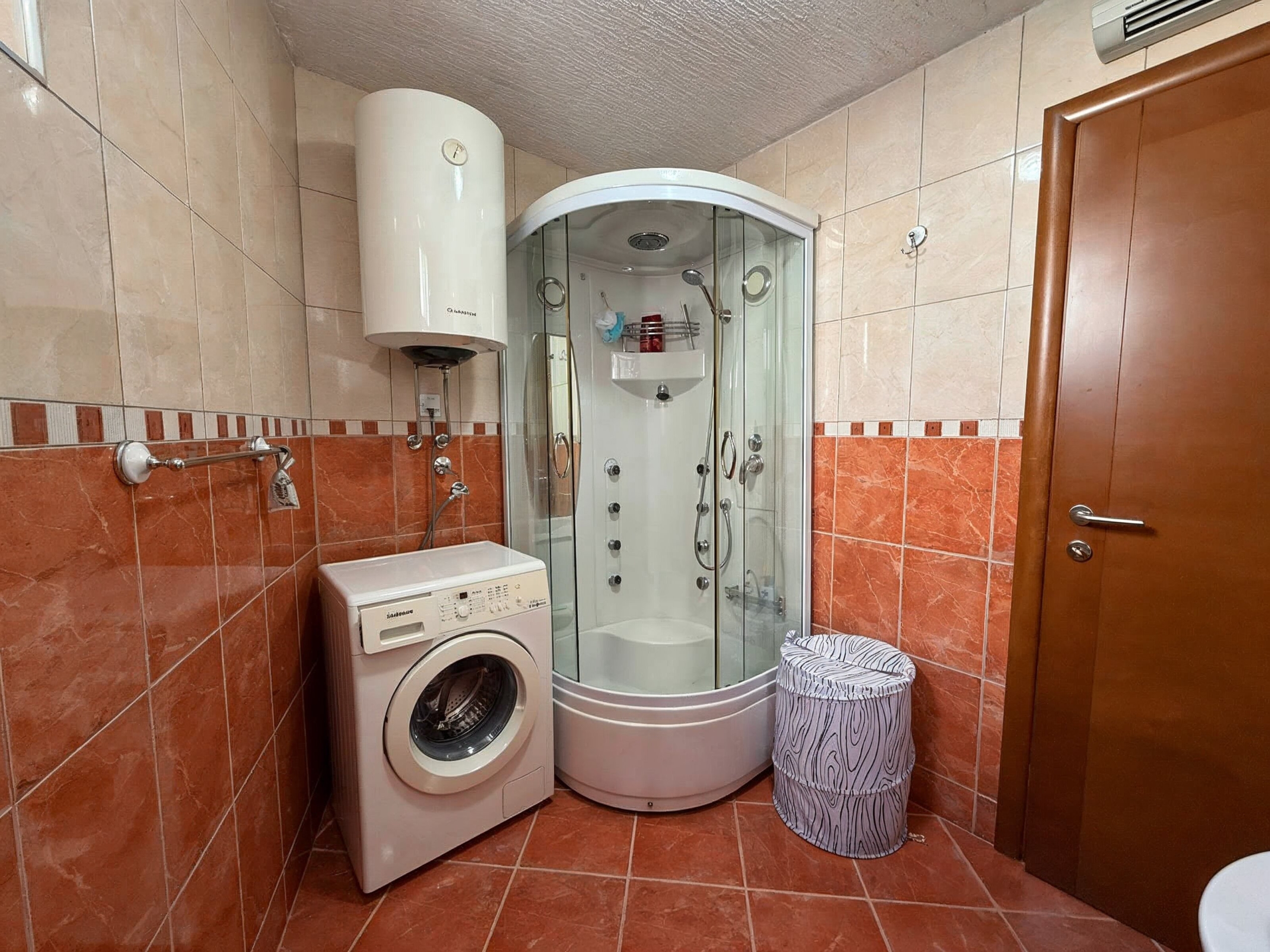 Badezimmer in einer Wohnung in Bečići, Montenegro: Duschkabine, Waschmaschine und Boiler, gefliest.