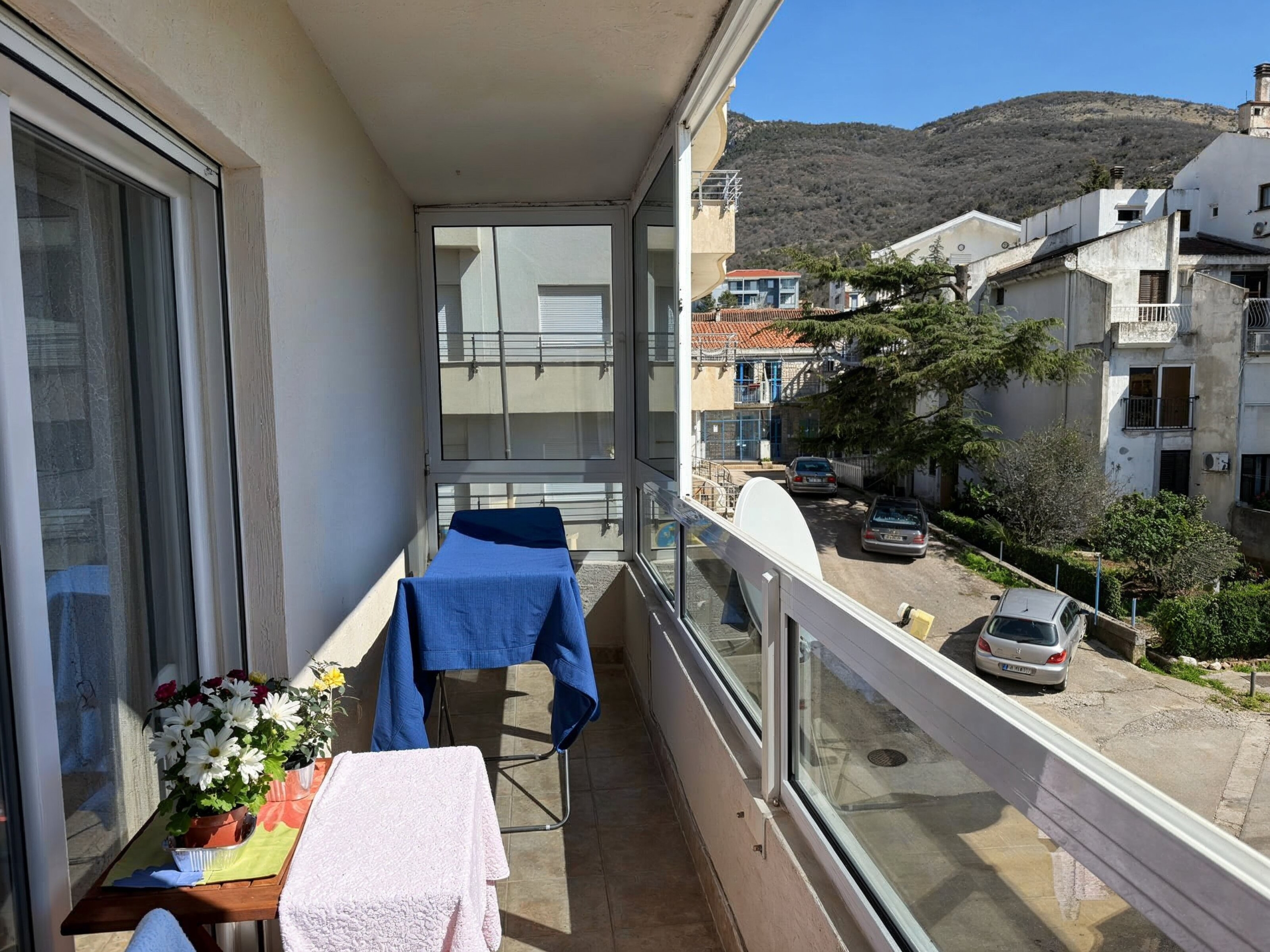 Verglaster Balkon in einer Wohnung in Bečići, Montenegro, mit Blick auf die Straße, die Berge und Wohnbebauung.