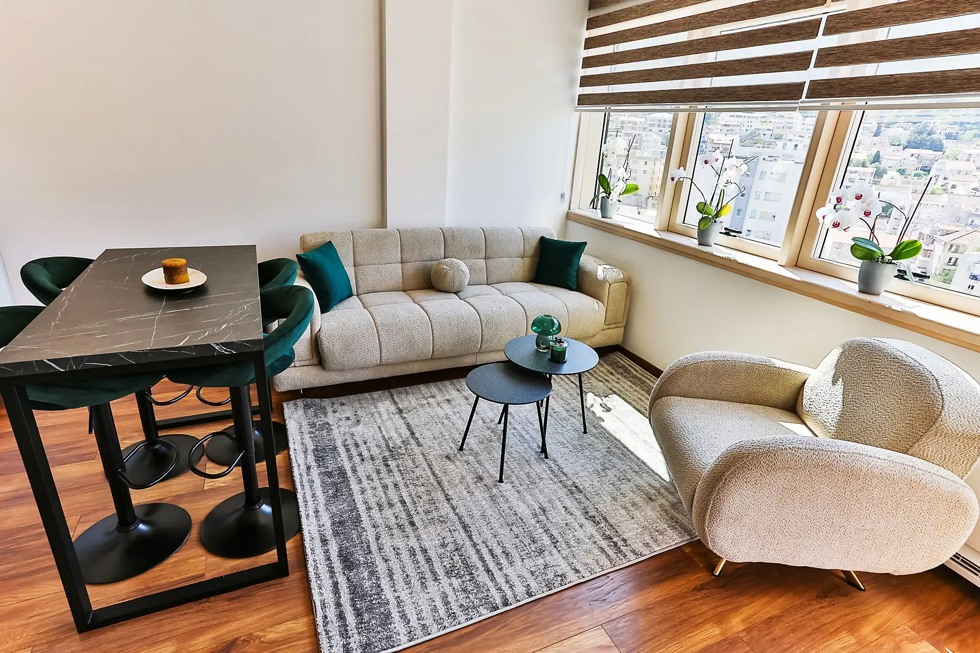 Modern living room with a beige sofa, green bar stools, and a black marble table near the window.