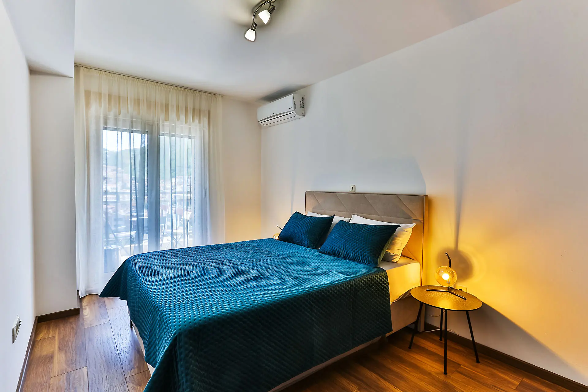 Modernes Schlafzimmer mit Doppelbett in einer Wohnung in Budva, Montenegro: Parkett, Klimaanlage und Zugang zum Balkon.