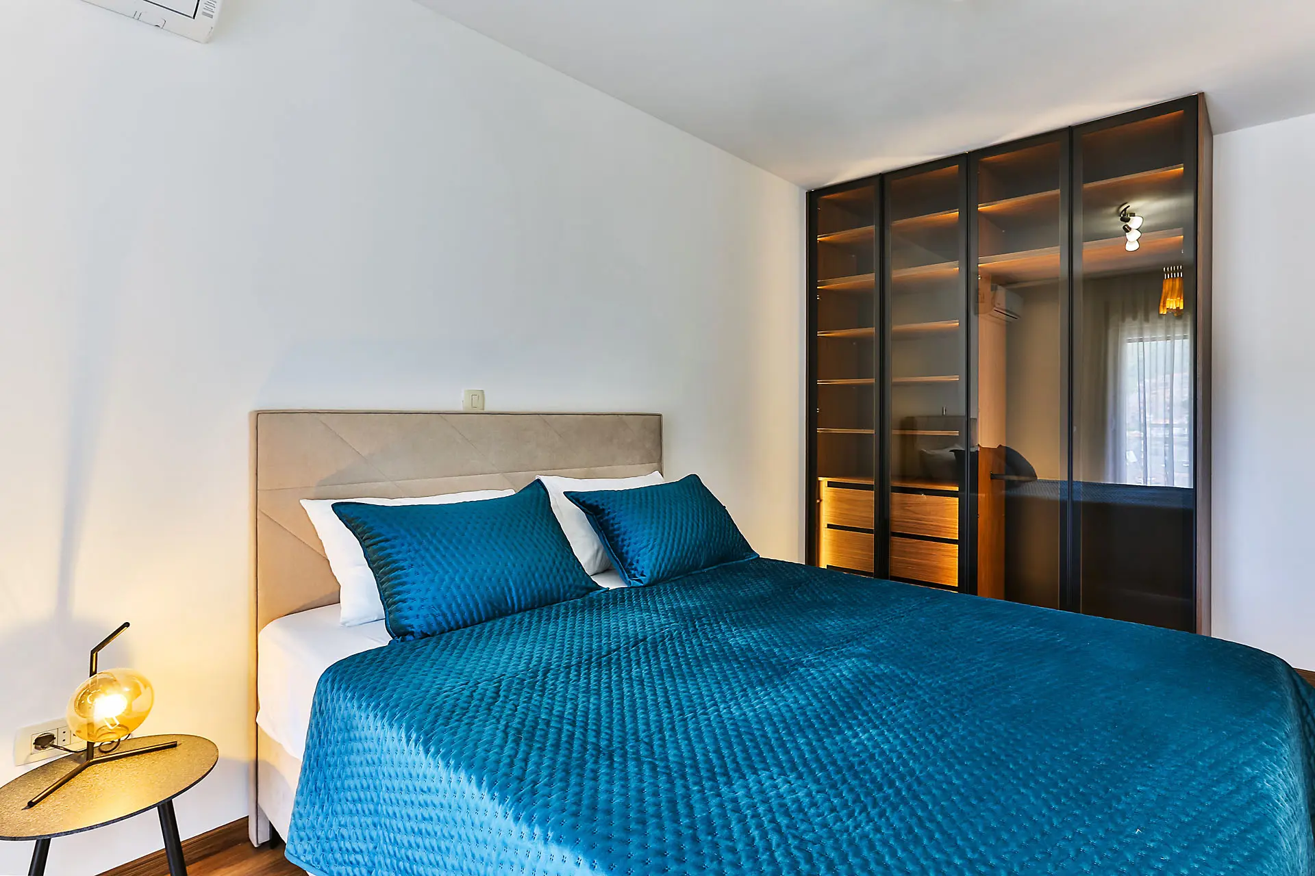 Modernes Schlafzimmer in einer Wohnung in Budva, Montenegro: Doppelbett, blaue Tagesdecke und beleuchteter Kleiderschrank.