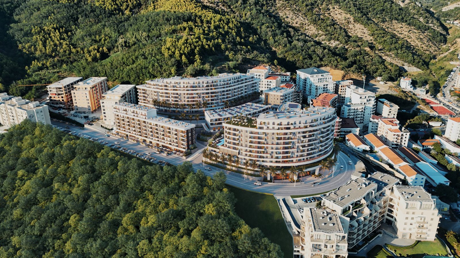Pogled iz vazduha na moderan stambeni kompleks u Bečićima, Crna Gora: višespratnice okružene planinama i zelenilom.