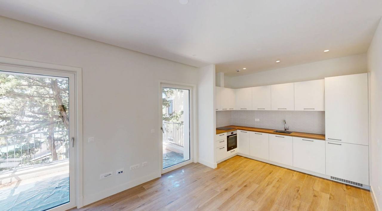 Moderne Küche in der Wohnung in Luštica, Montenegro: weiße Fronten, Holzarbeitsplatte und Zugang zur Terrasse.