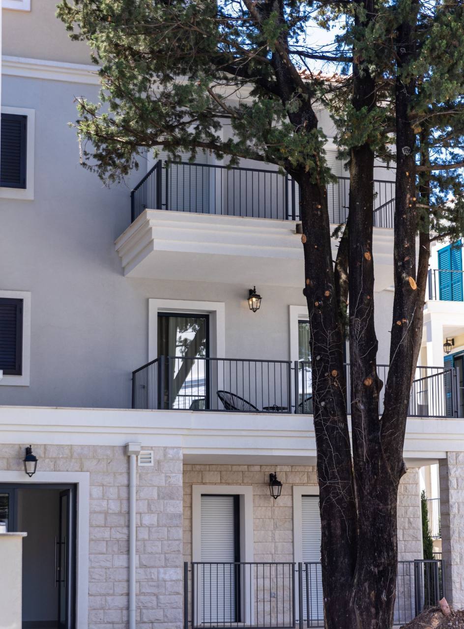 Fassade einer modernen Wohnung in Luštica Bay, Montenegro: helle Fassade, Steinsockel, Balkone und Blick auf Zypressen.