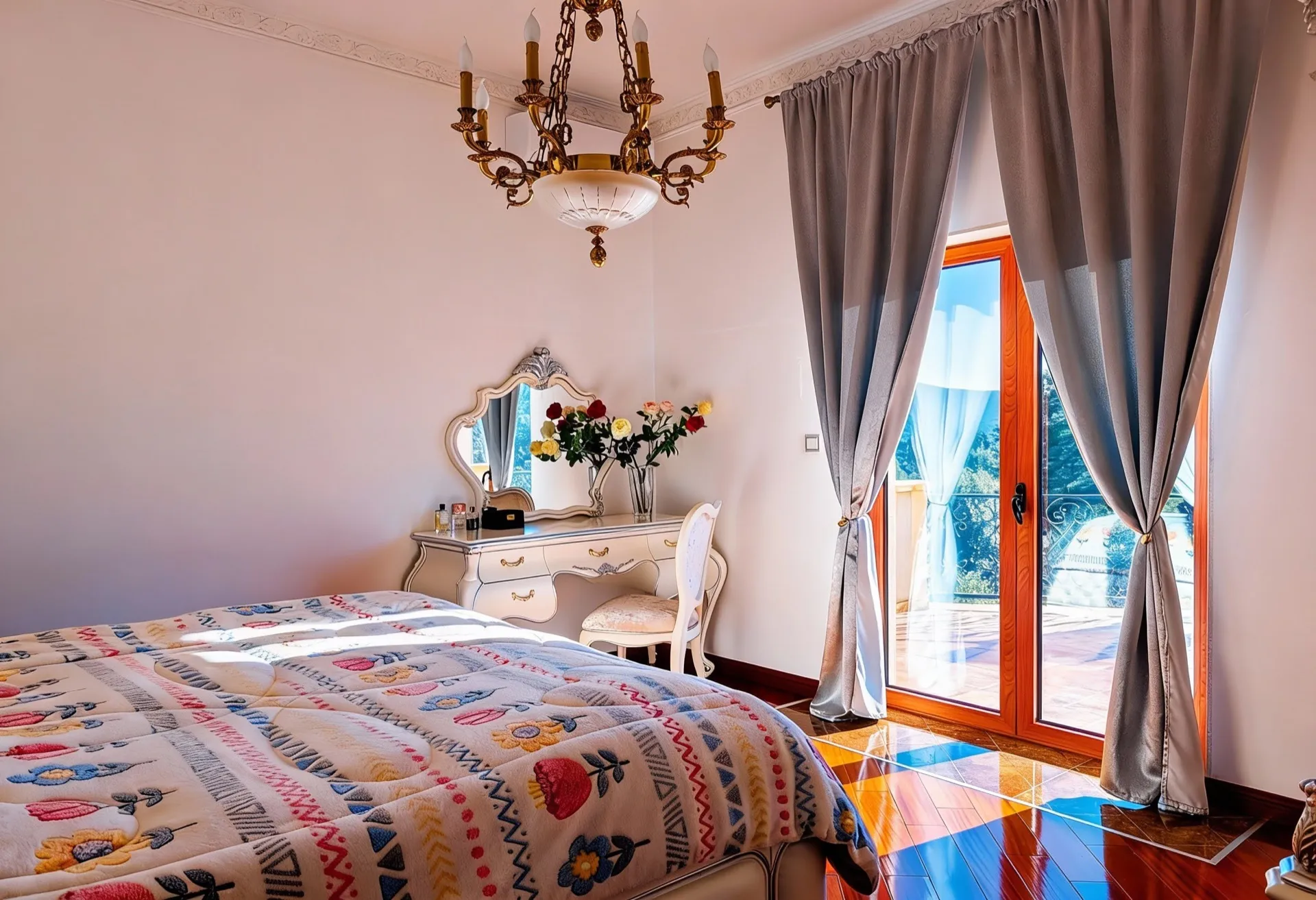 Hell Schlafzimmer mit farbenfroher Decke, weißer Kommode, verziertes Spiegel und klassischer Kronleuchter neben grauen Vorhängen.