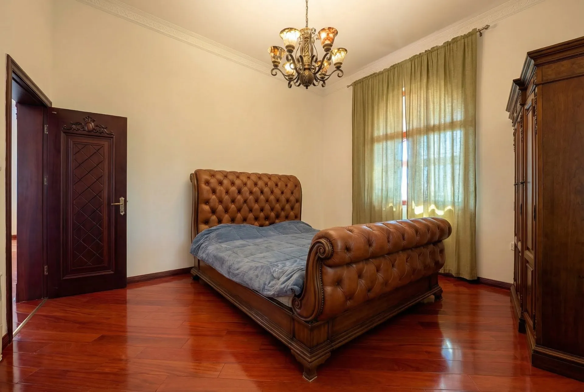 Schlafzimmer mit einem großen gepolsterten Lederbett, glänzendem Holzboden und einer klassischen Kronleuchter.