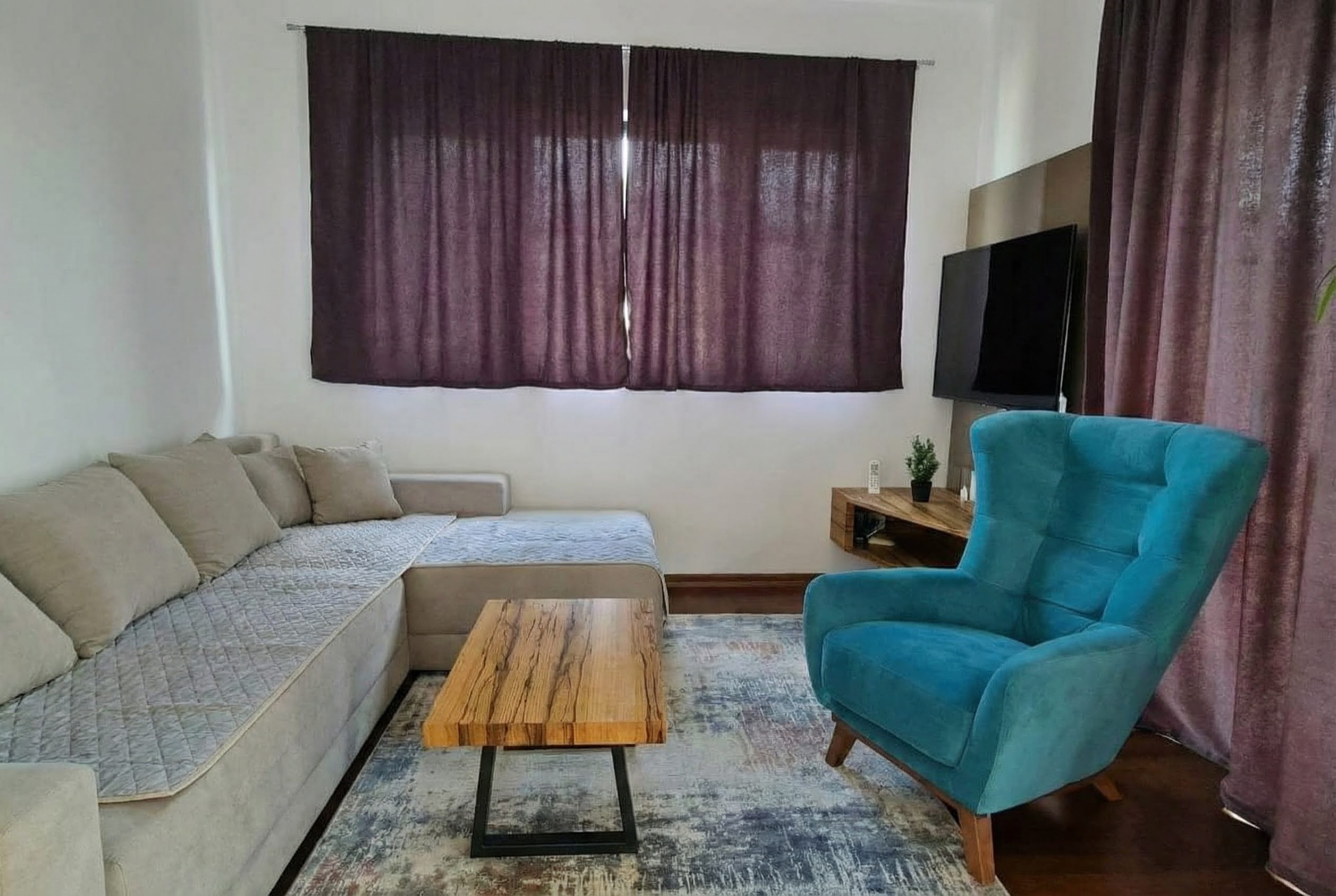 Gemütliches Wohnzimmer in einer Wohnung in Bečići, Montenegro: graues Ecksofa, türkisfarbener Sessel und ein Couchtisch aus Holz.