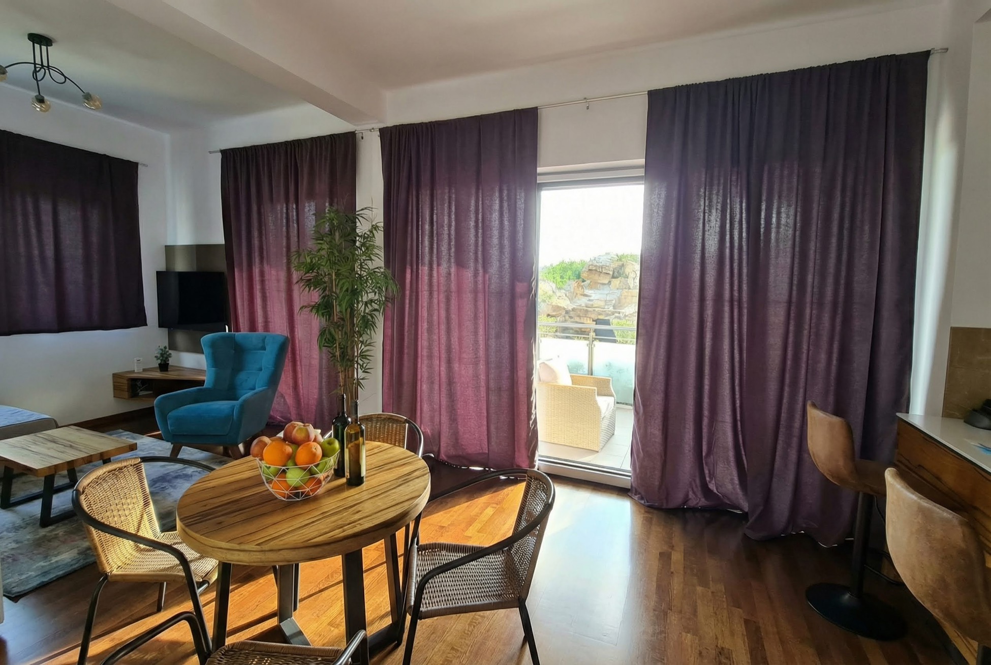 Wohnzimmer in einem Apartment in Bečići, Montenegro: Essbereich, blauer Sessel, Zugang zur Terrasse mit Bergblick.