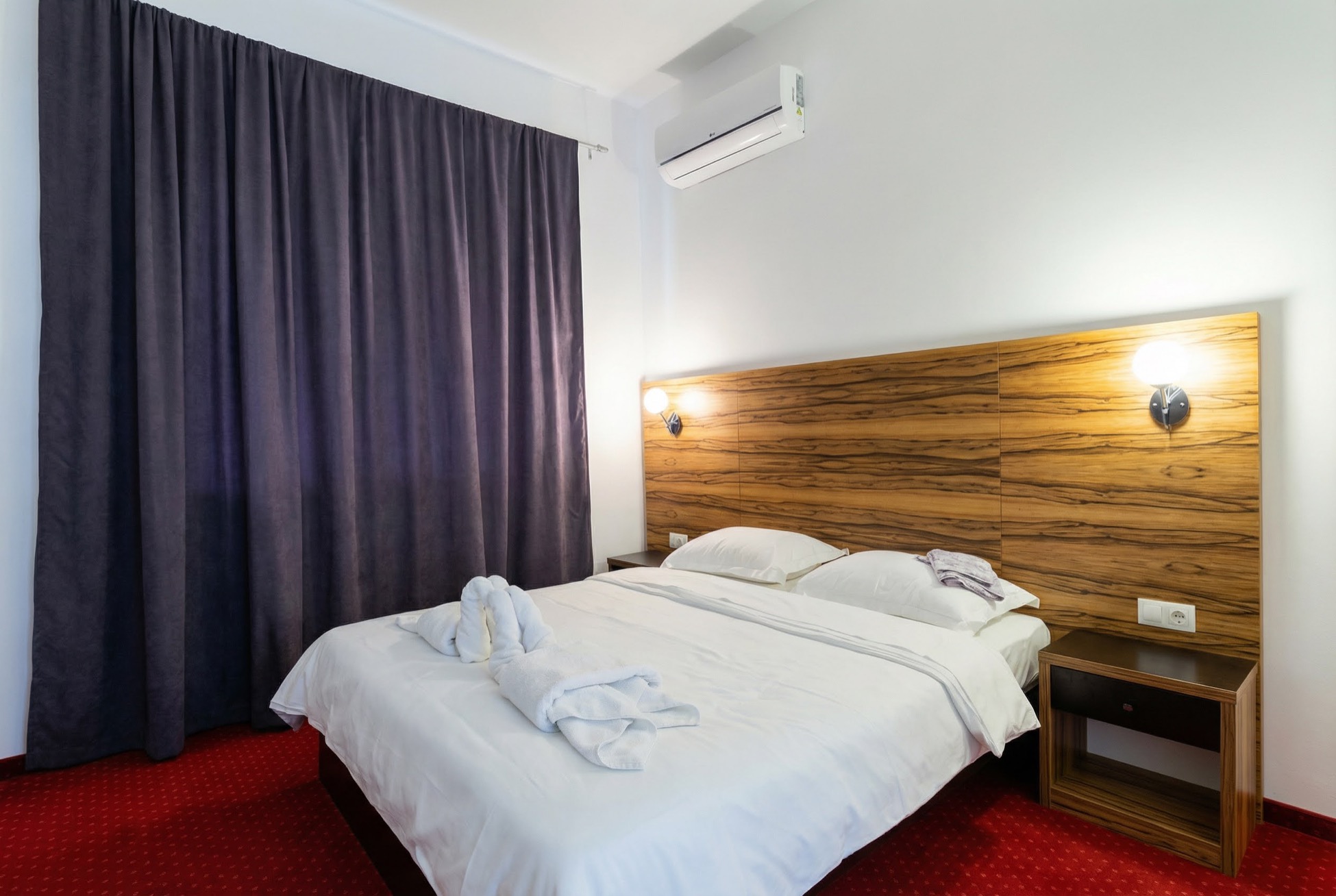 Schlafzimmer in einem Apartment in Bečići, Montenegro: Doppelbett mit Holzkopfteil, Klimaanlage und dunkle Vorhänge.