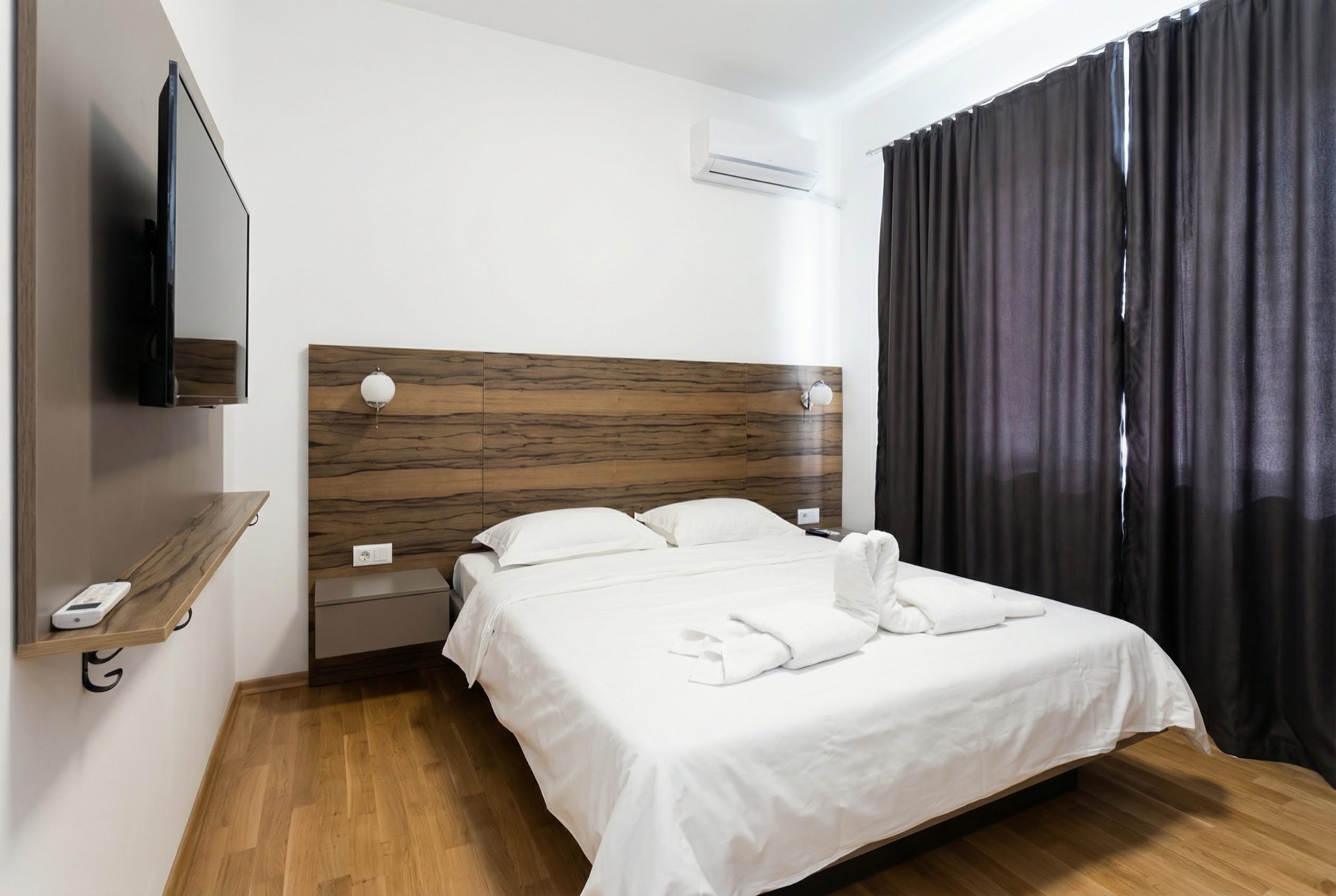 Modernes Schlafzimmer in einer Wohnung in Bečići, Montenegro: Doppelbett, hölzernes Kopfteil, TV und Klimaanlage.