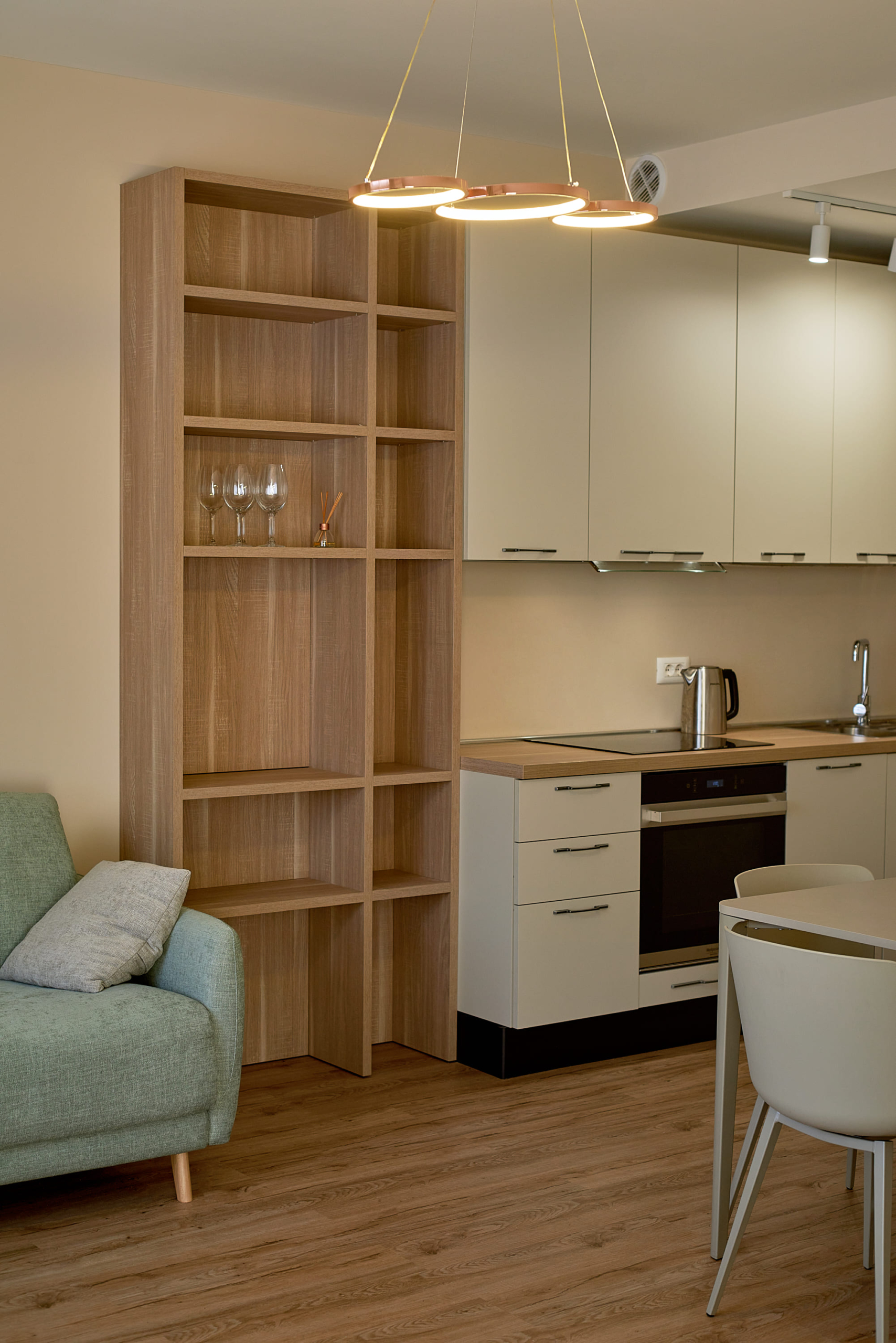 Cuisine-salon moderne dans un appartement à Bečići, Monténégro : meuble de cuisine clair, étagère en bois et fauteuil menthe.
