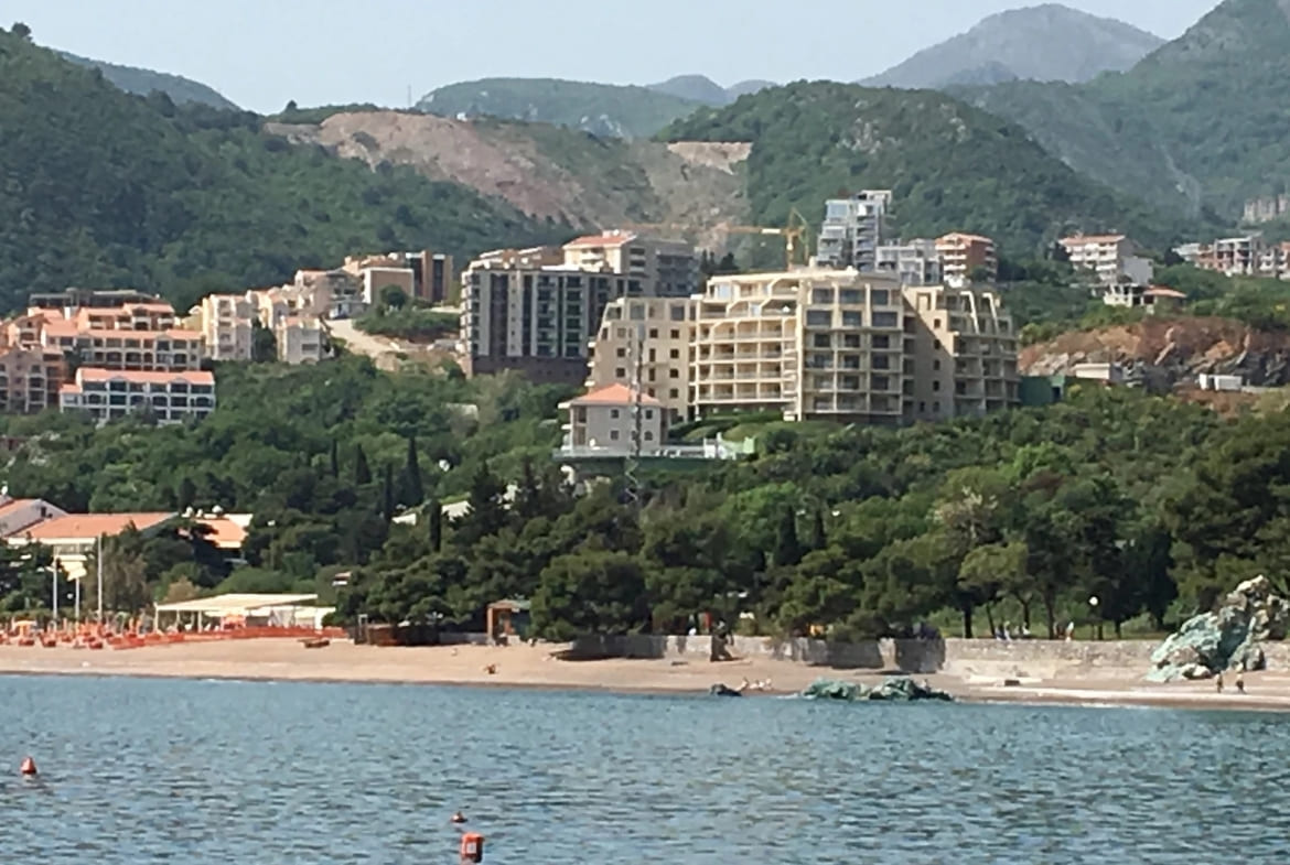 Vue sur le complexe résidentiel et la plage de sable à Bečići, Monténégro, avec en toile de fond les montagnes verdoyantes et le littoral.