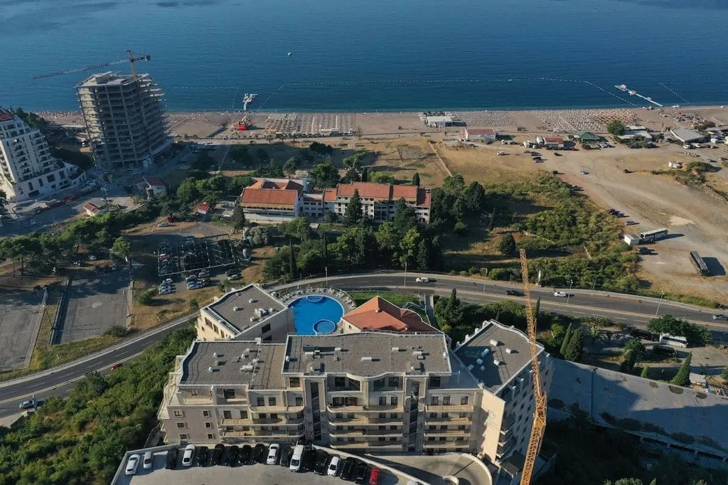 Vue aérienne d'une ville côtière avec un bâtiment à plusieurs étages, une piscine sur le toit et une plage.