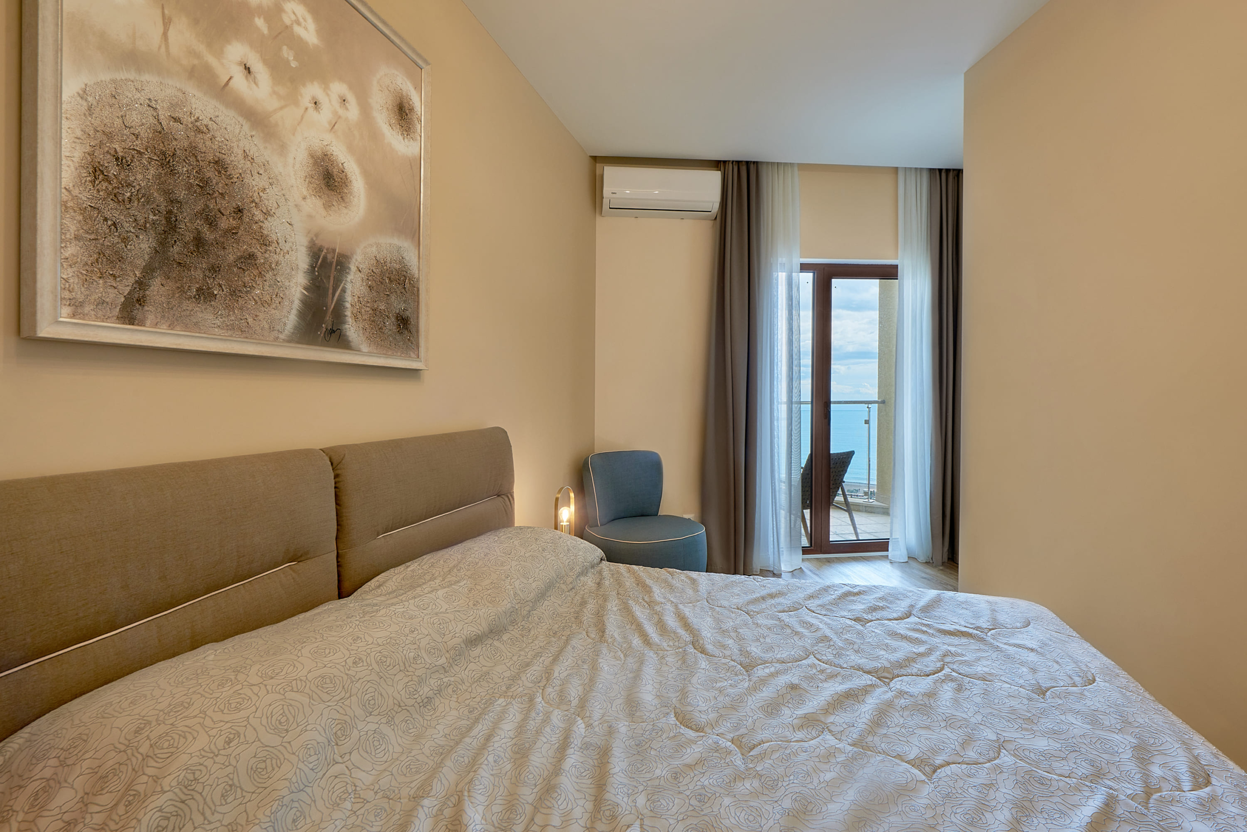 Chambre dans un appartement à Bečići, Monténégro : lit double, fauteuil et accès au balcon avec vue sur la mer.