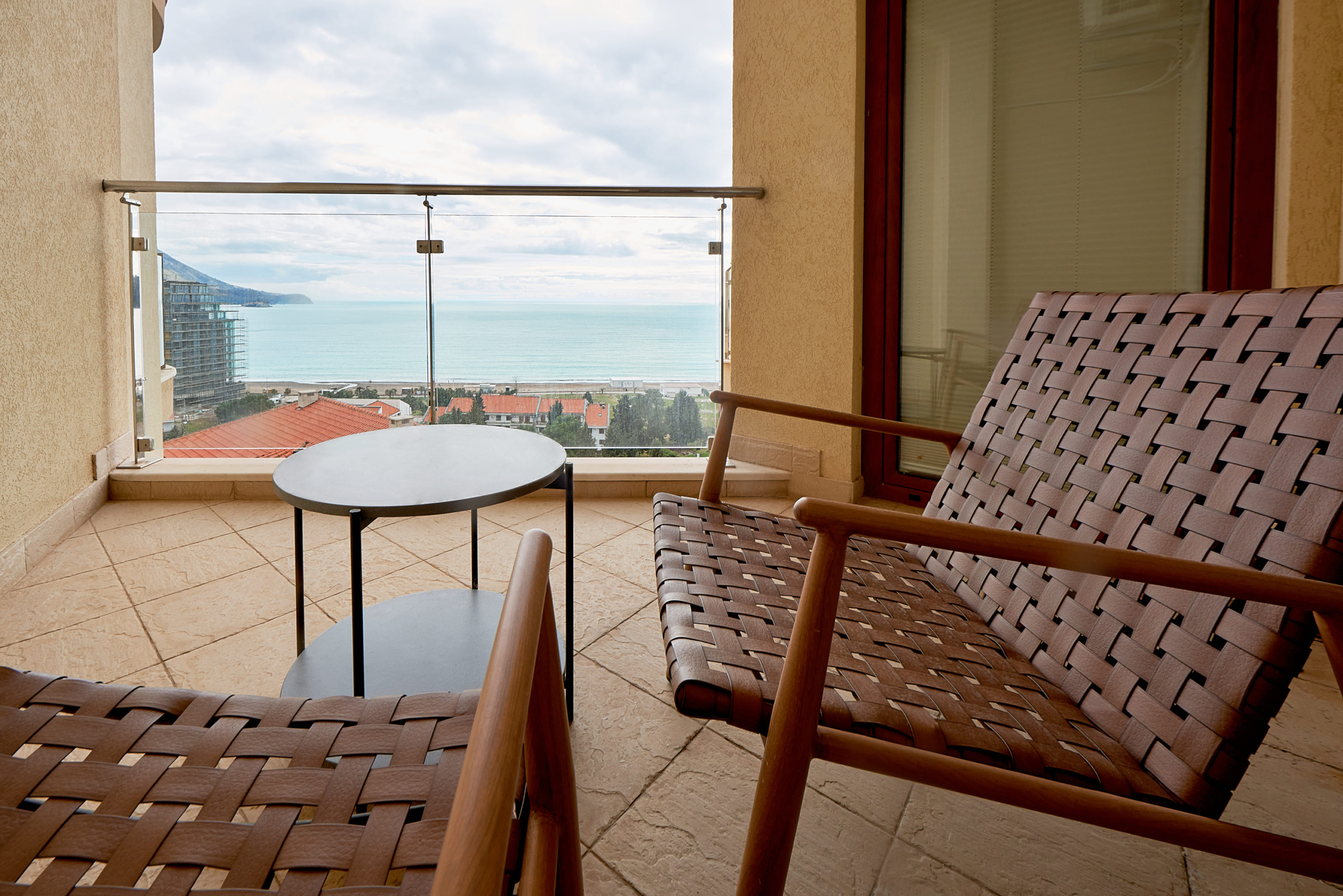 Balcon avec fauteuils en osier et vue sur la mer dans un appartement, Bečići, Monténégro. Terrasse moderne avec vue panoramique.