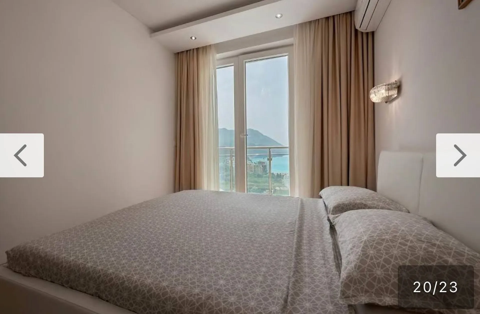 Chambre lumineuse avec grand lit et fenêtre panoramique. Vue sur la mer et les montagnes. Rideaux beige, tête de lit blanche, climatisation.
