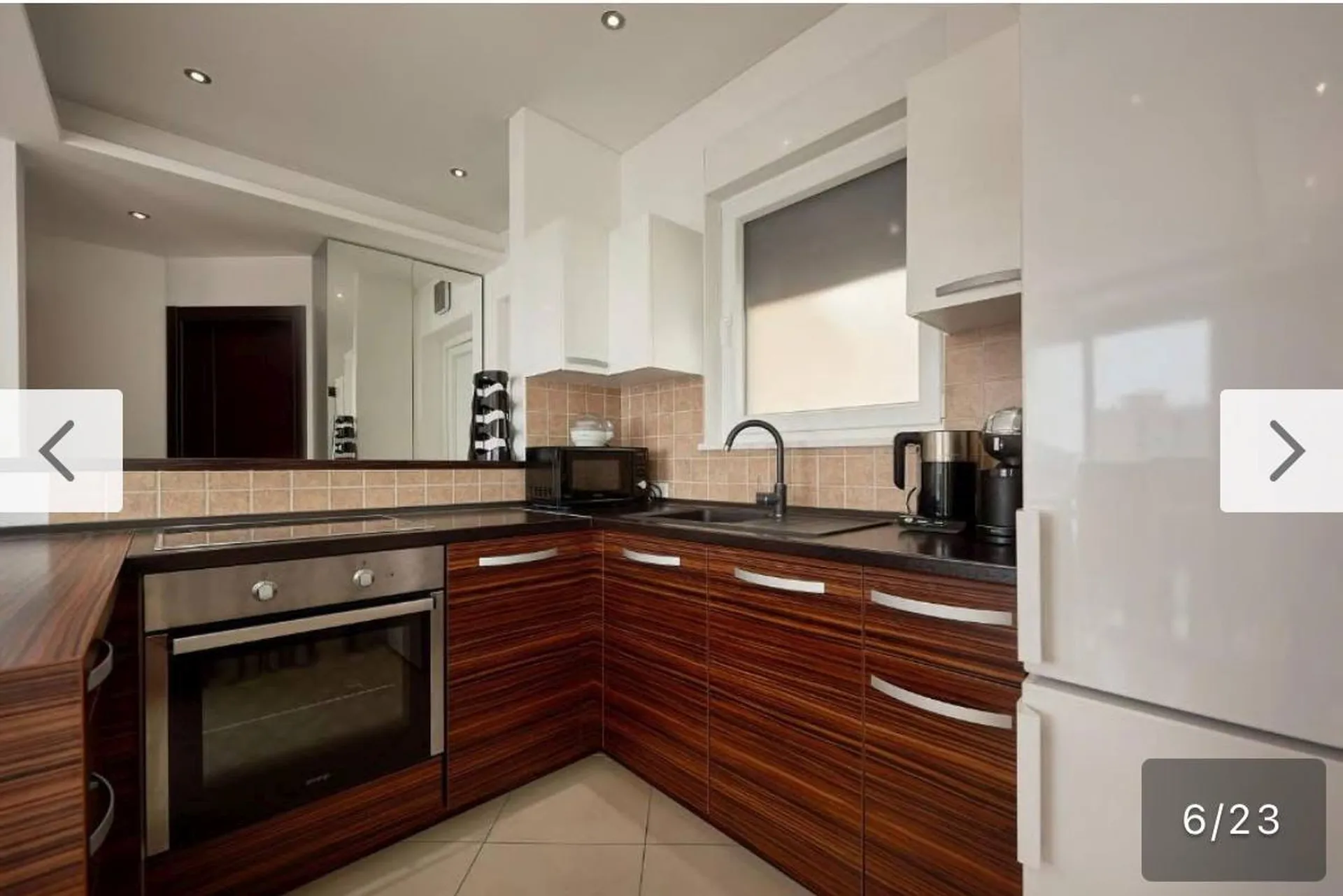 Cuisine moderne avec meubles en bois foncé, four intégré, micro-ondes et réfrigérateur blanc près d'une fenêtre.