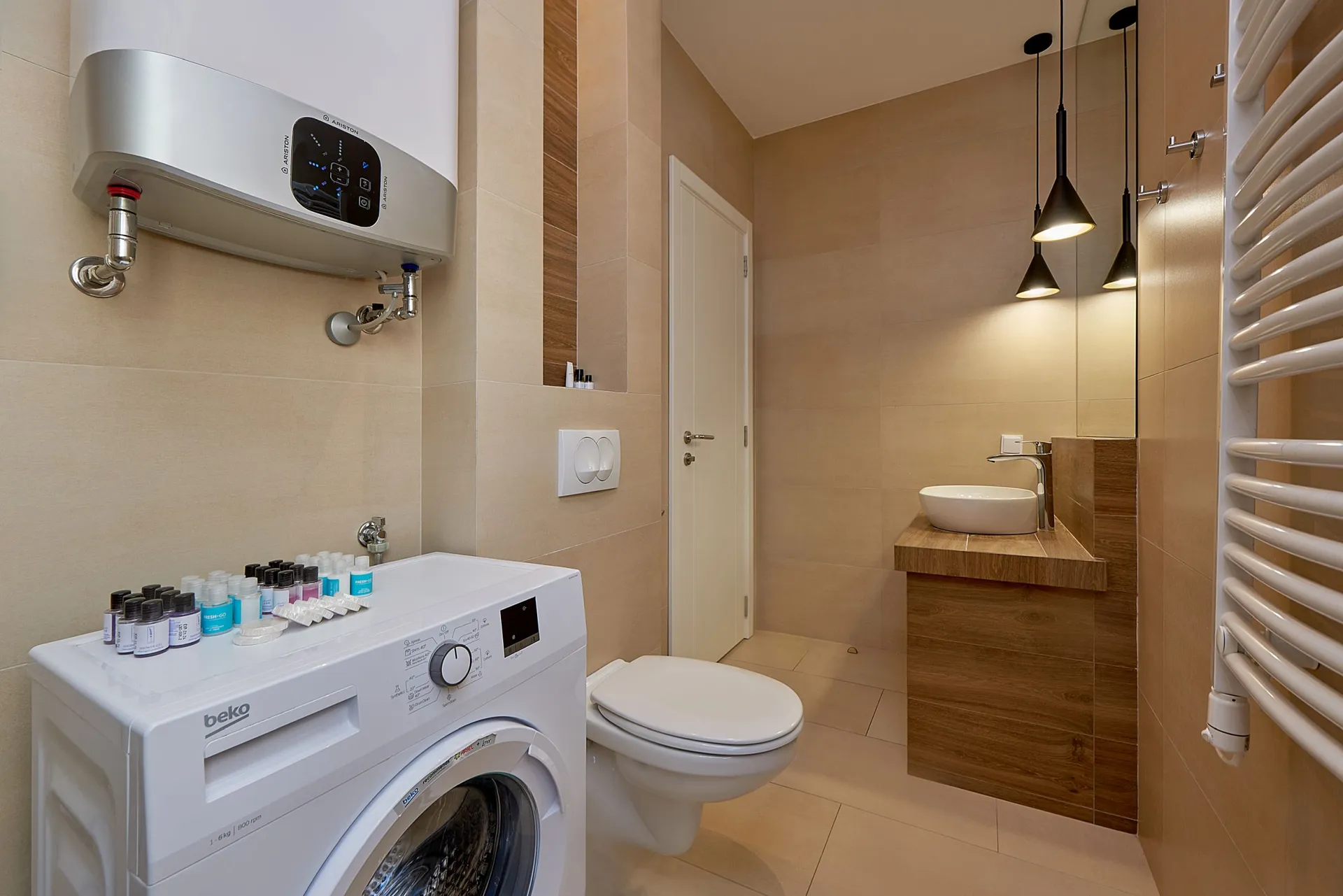 Moderne Baderum mit Waschmaschine, wandmontierter Toilette und Aufsatzwaschbecken auf Holzschrank.