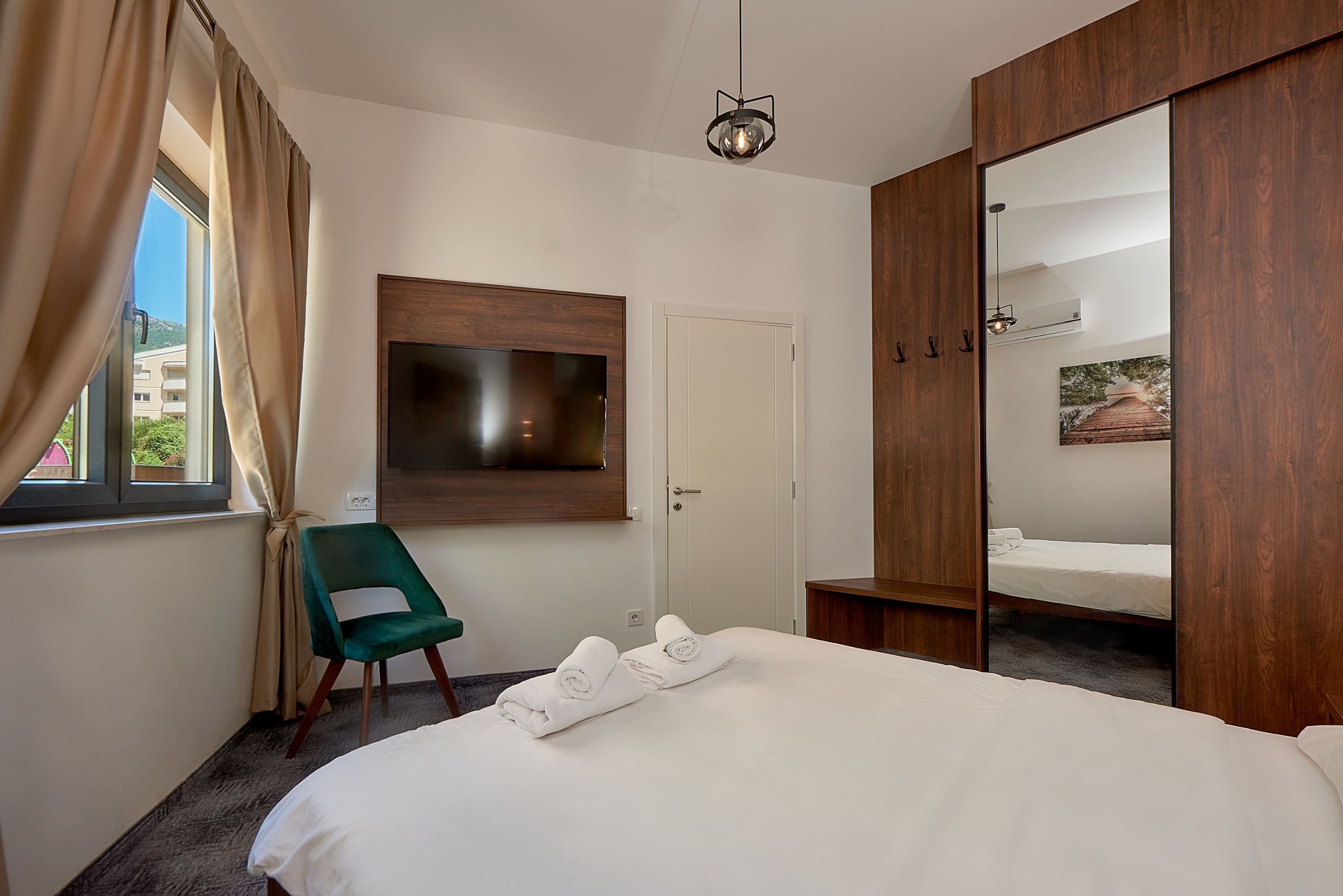 Chambre moderne dans un appartement à Bečići, Monténégro : lit double, armoire miroir et vue depuis la fenêtre.