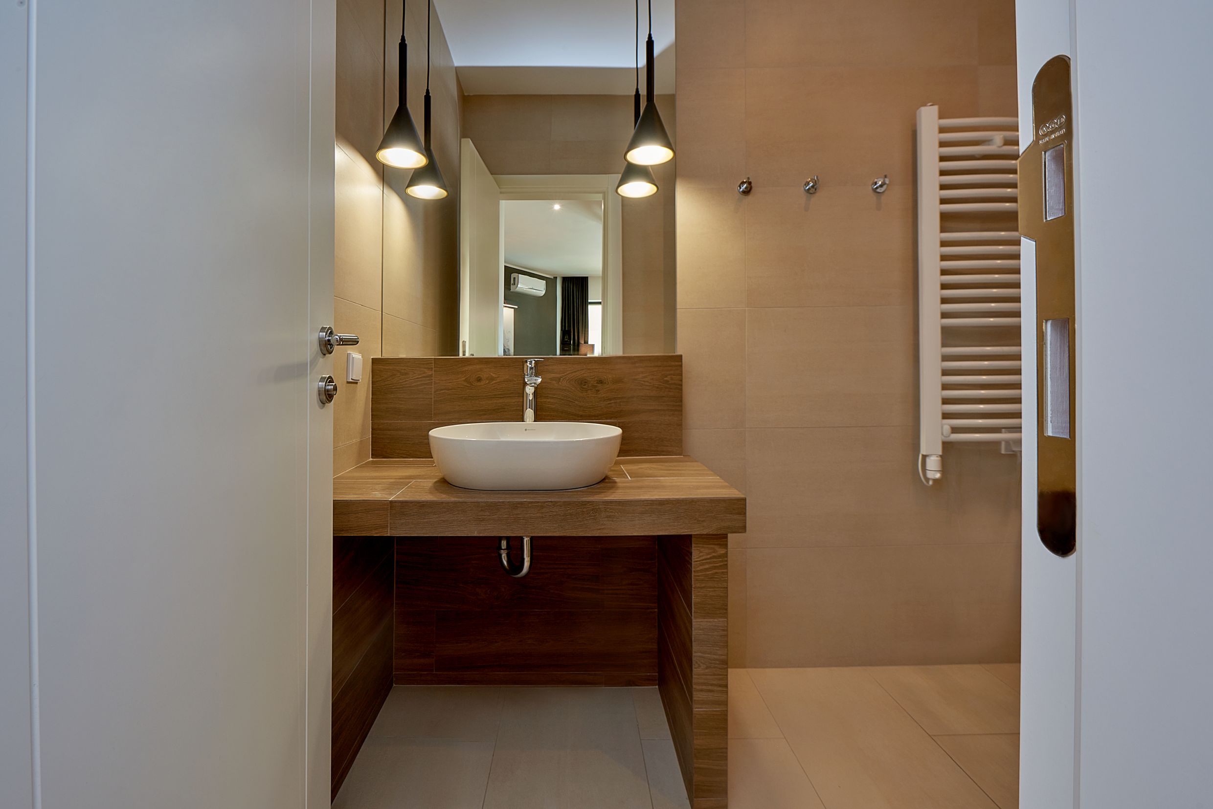 Salle de bain moderne dans un appartement à Bečići, Monténégro : vasque à poser, finition imitation bois et sèche-serviettes.