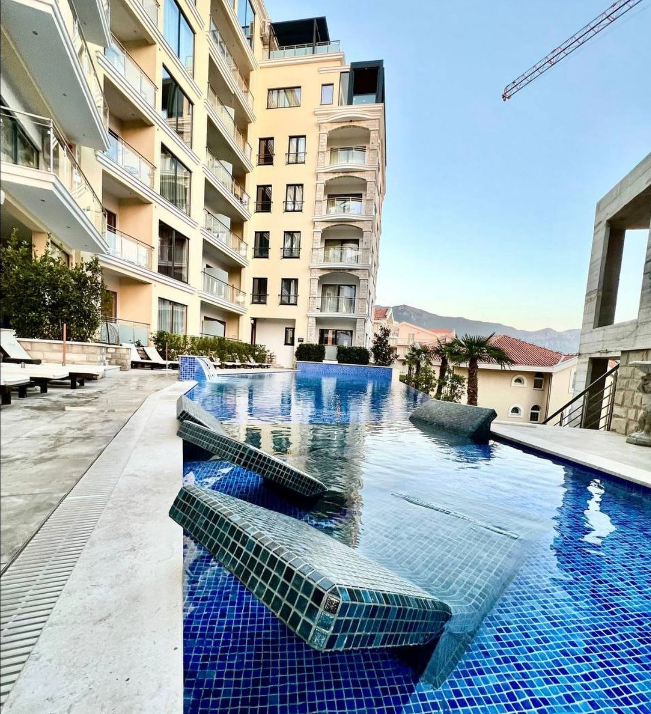Piscine extérieure avec transats dans un complexe résidentiel moderne à Bečići, Monténégro. Vue sur un immeuble de plusieurs étages et les montagnes.