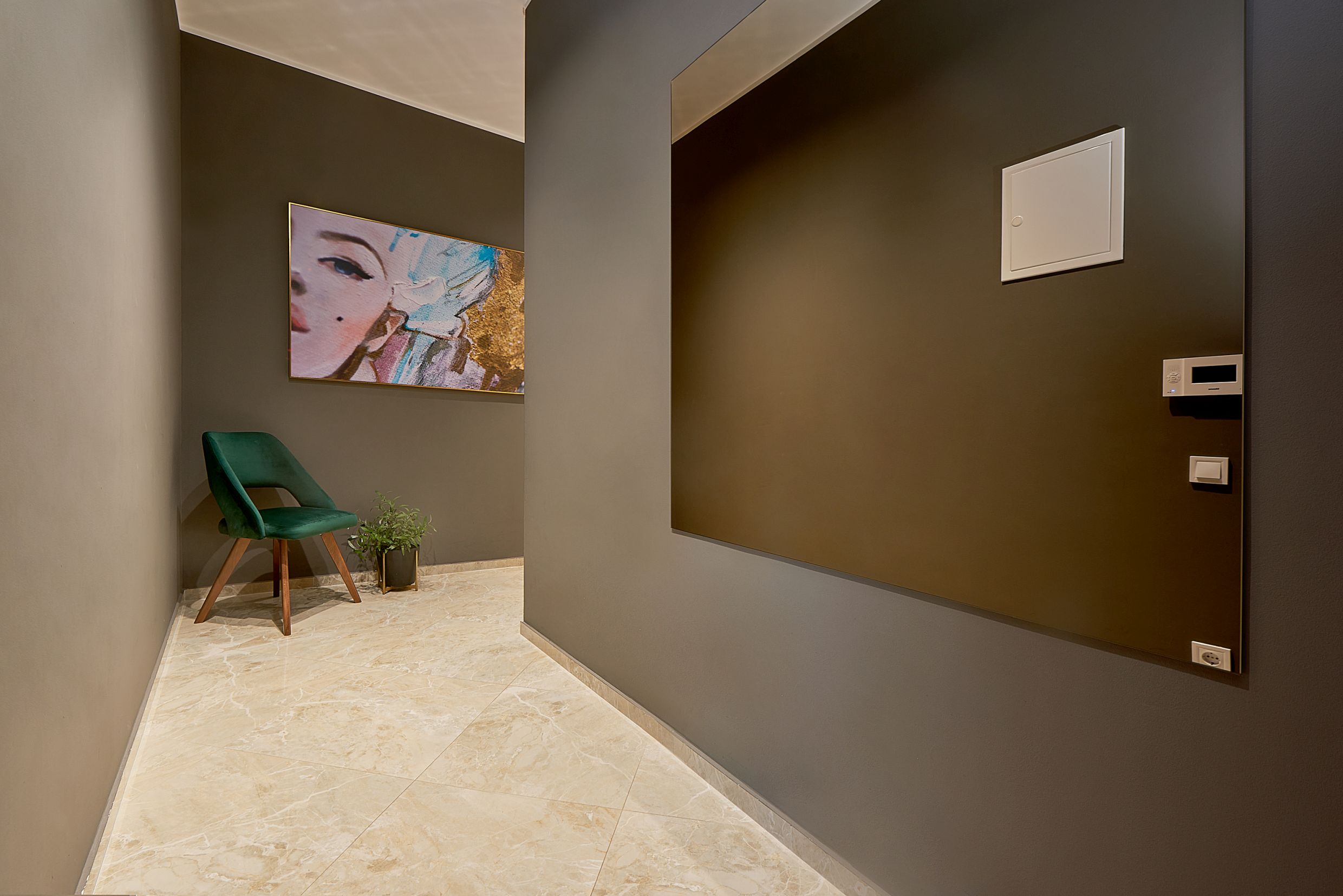 Intérieur moderne d’une entrée d’appartement à Bečići, Monténégro : finitions grises, fauteuil vert et miroir mural.