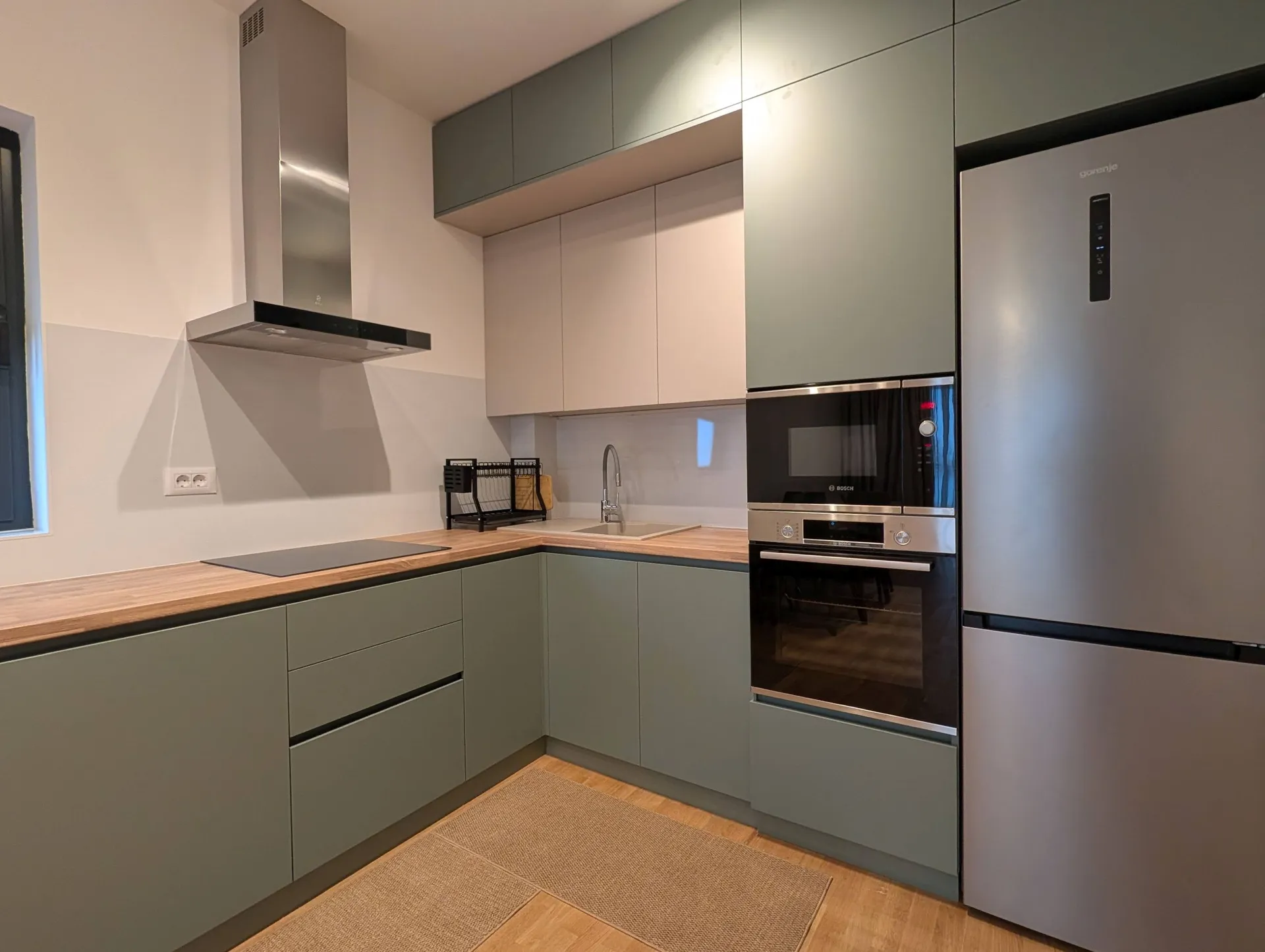 Moderne Küche mit grünen Schränken, Holzarbeitsplatte, eingebautem Ofen und Edelstahl-Kühlschrank.