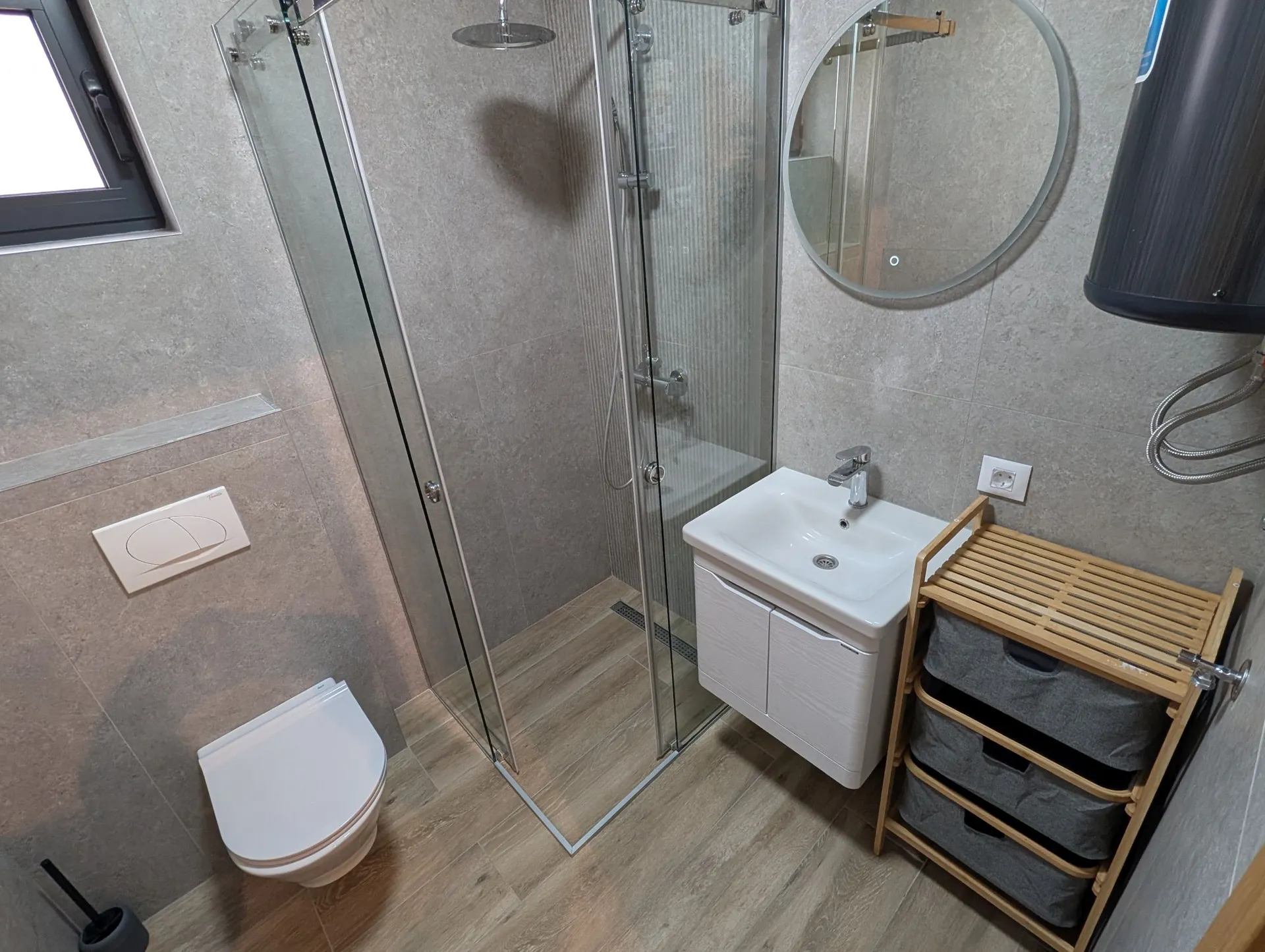 Moderne Dusche mit Glaswand, Wand-WC, Spülbecken und grauen Fliesen an den Wänden.