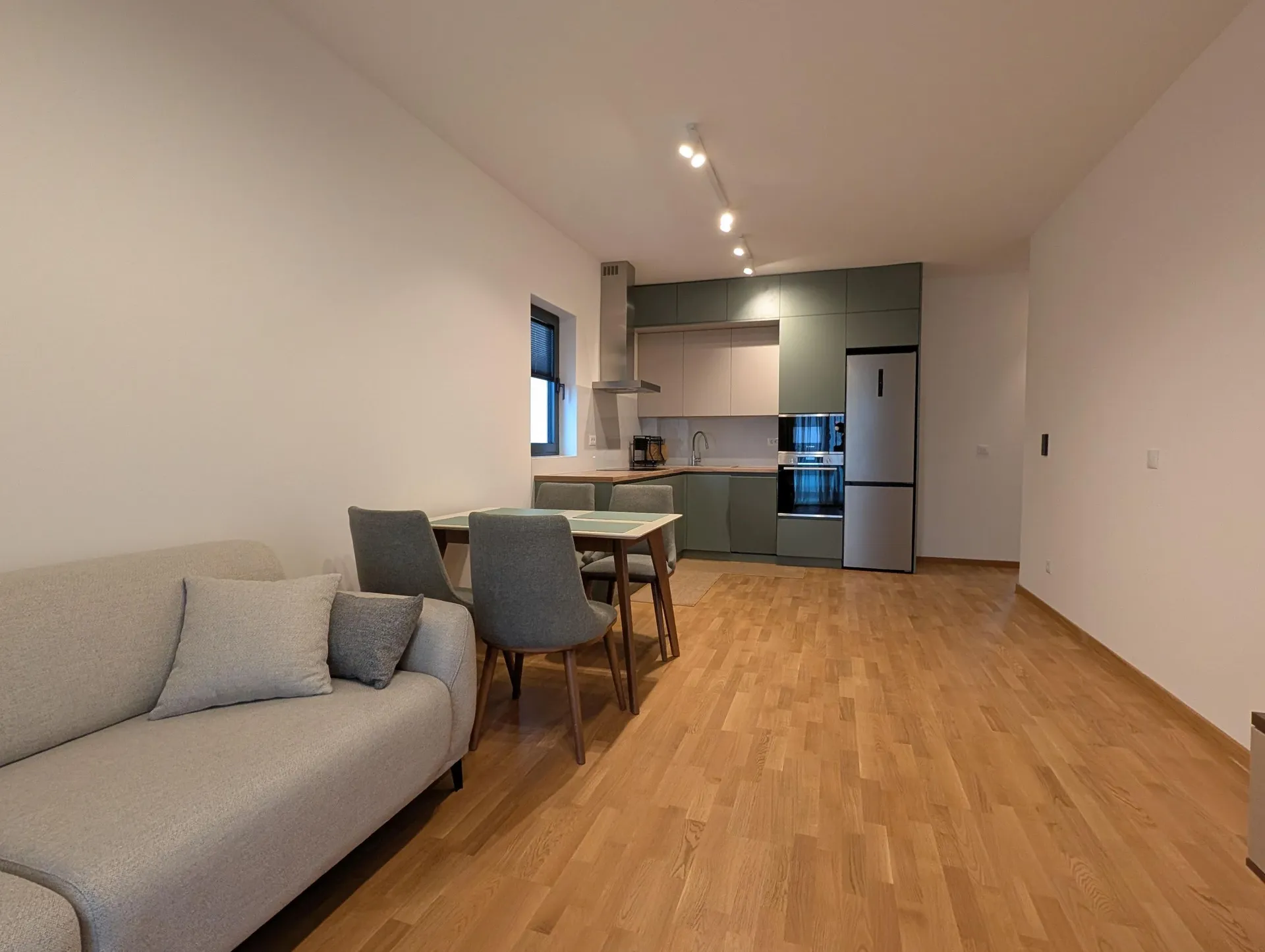 Moderne Studio-Wohnung mit grauem Sofa, Esstisch und grüner Küche auf hellem Holzboden.