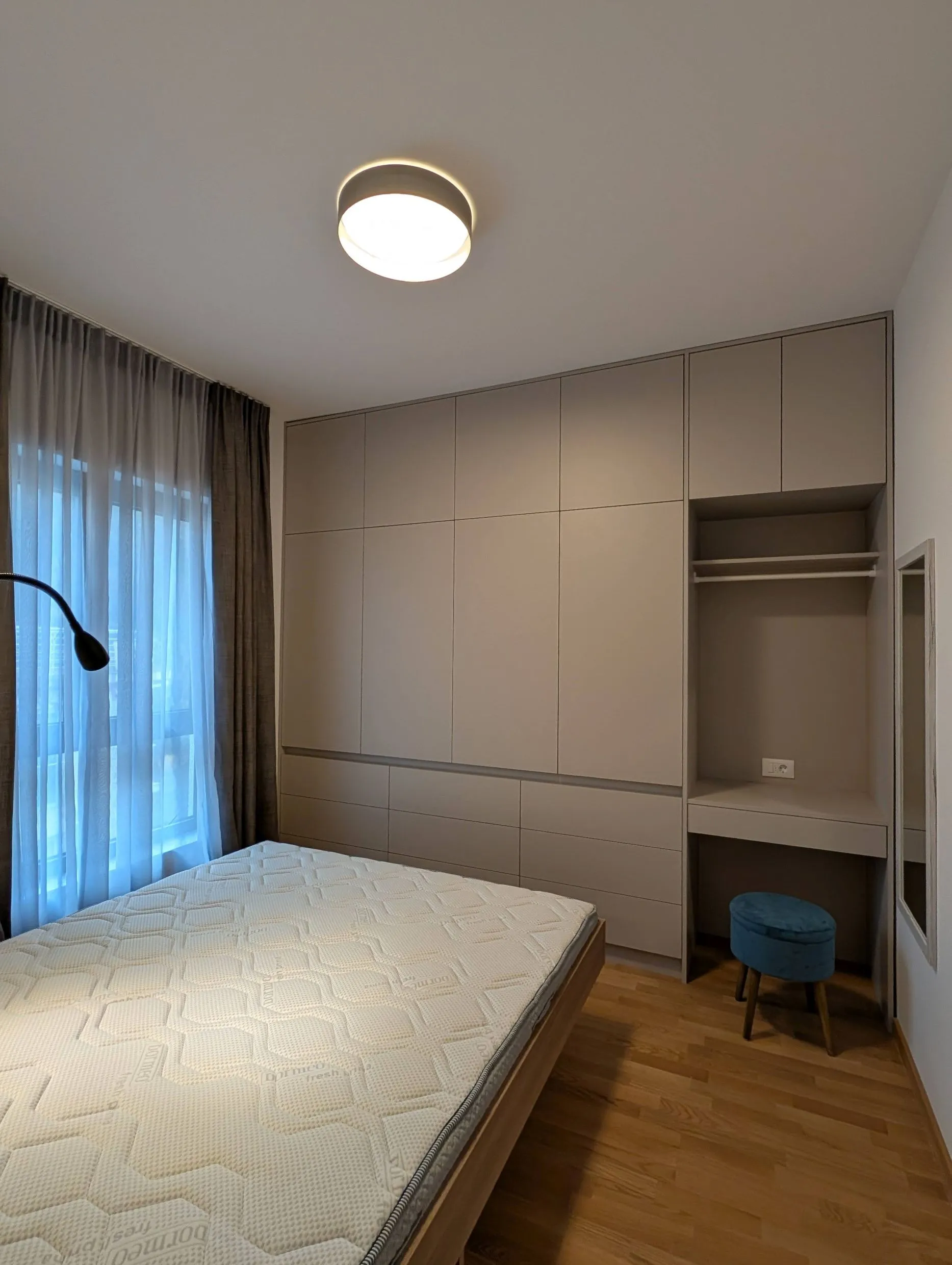 Moderne Schlafzimmer mit Matratze, Einbauschrank und blauem Hocker neben dem Fenster