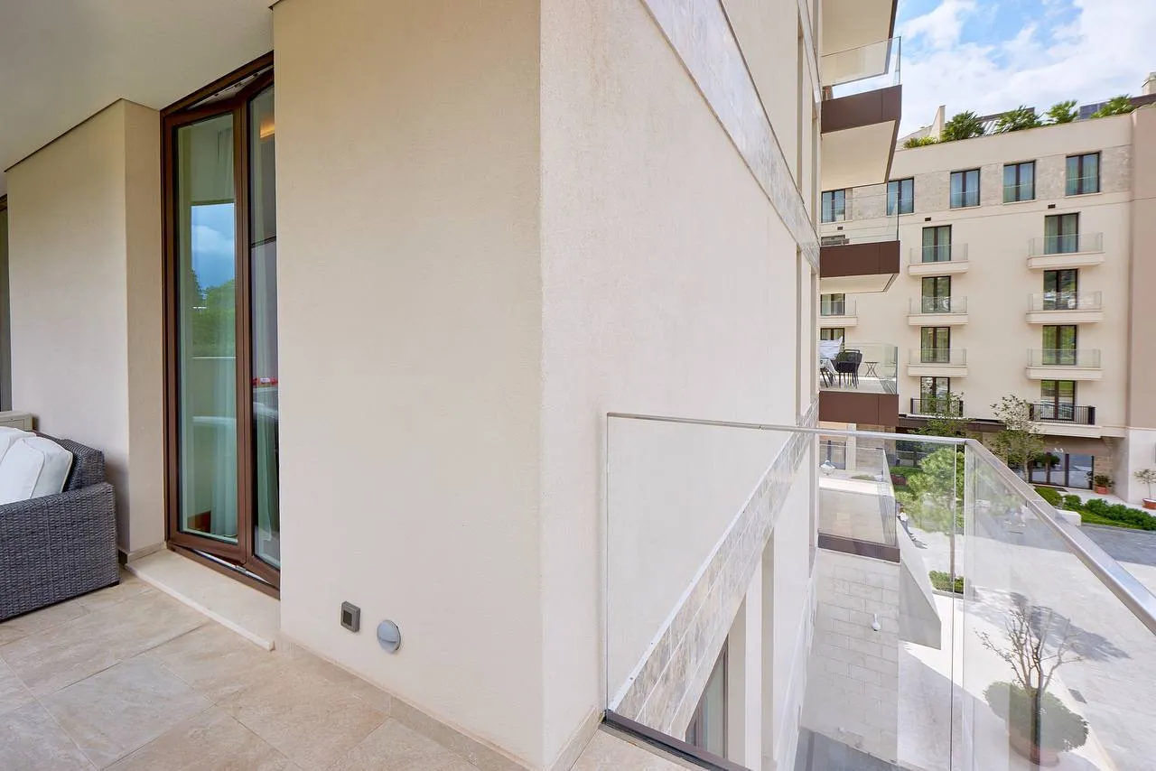 Moderne Terrasse mit transparenter Glasabgrenzung und Korbmöbeln. Blick auf den Innenhof und angrenzende Gebäude.