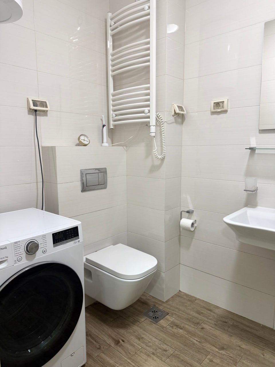 Salle de bain moderne dans un appartement à Podgorica, Monténégro : carrelage blanc, toilettes suspendues et machine à laver.