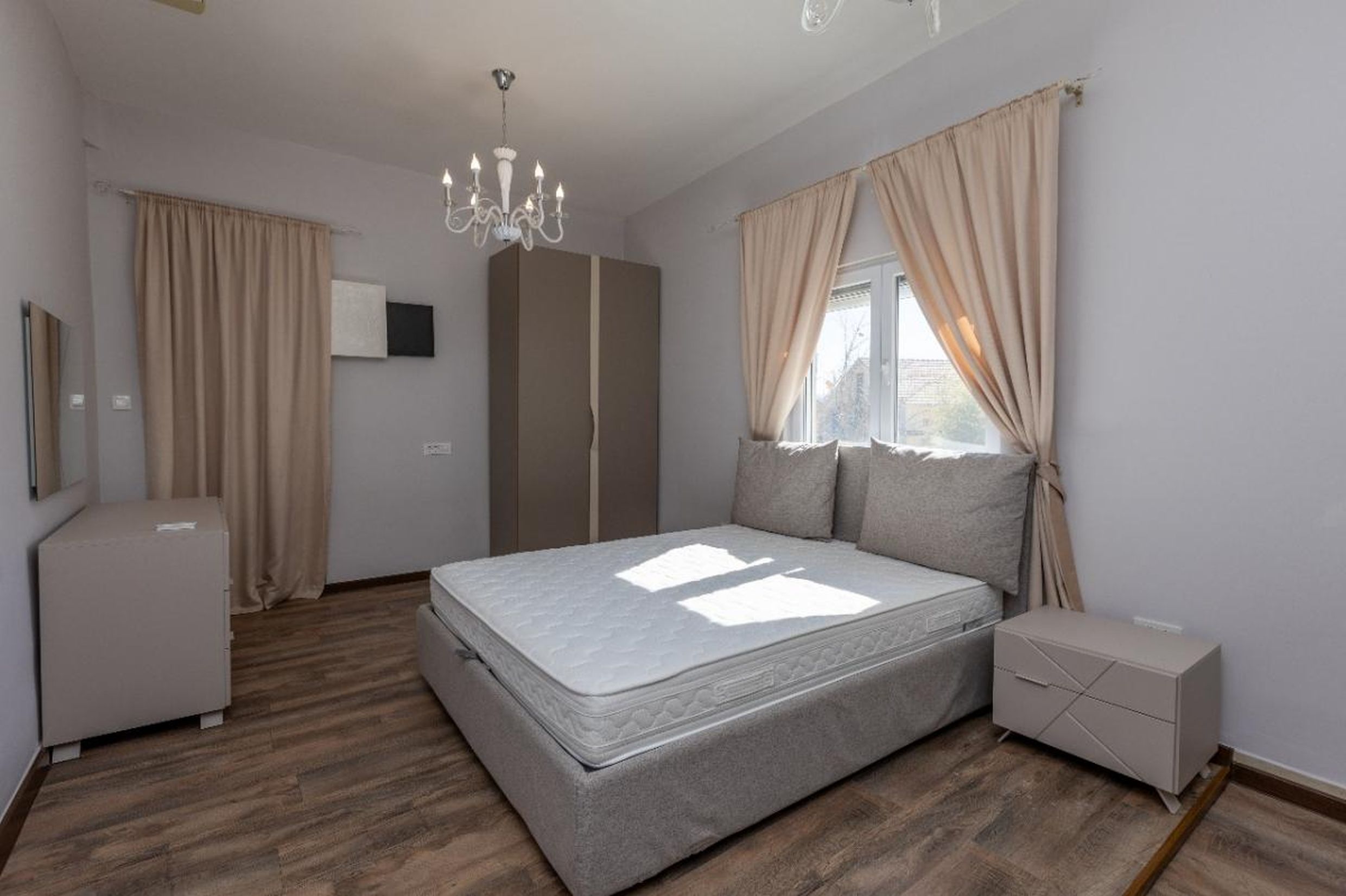 Chambre lumineuse dans une maison à Tivat, Monténégro : lit double, armoire, commode, parquet stratifié et lustre classique.