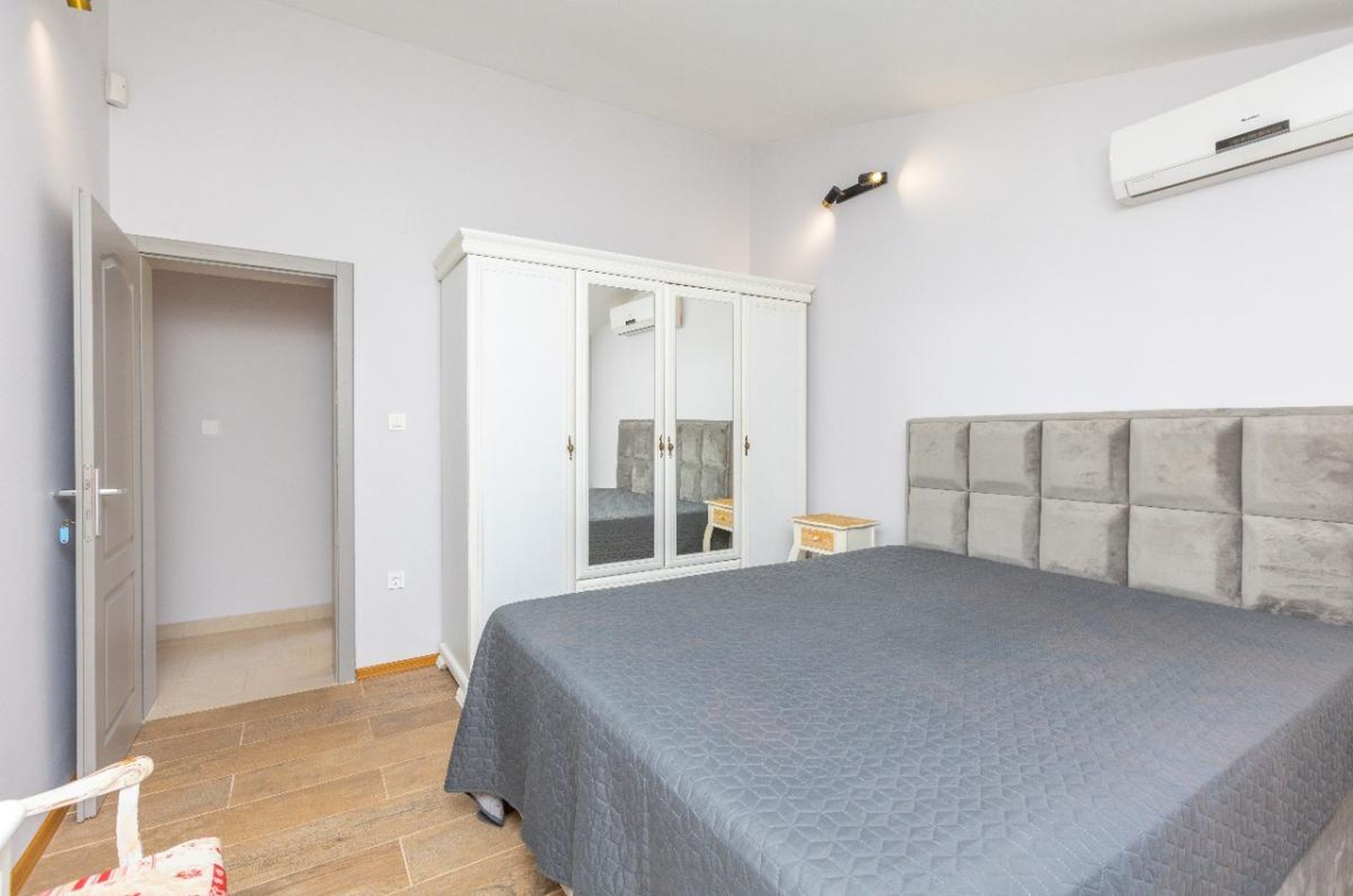 Chambre lumineuse dans une maison à Tivat, Monténégro : lit double avec tête de lit rembourrée, armoire blanche et climatisation.