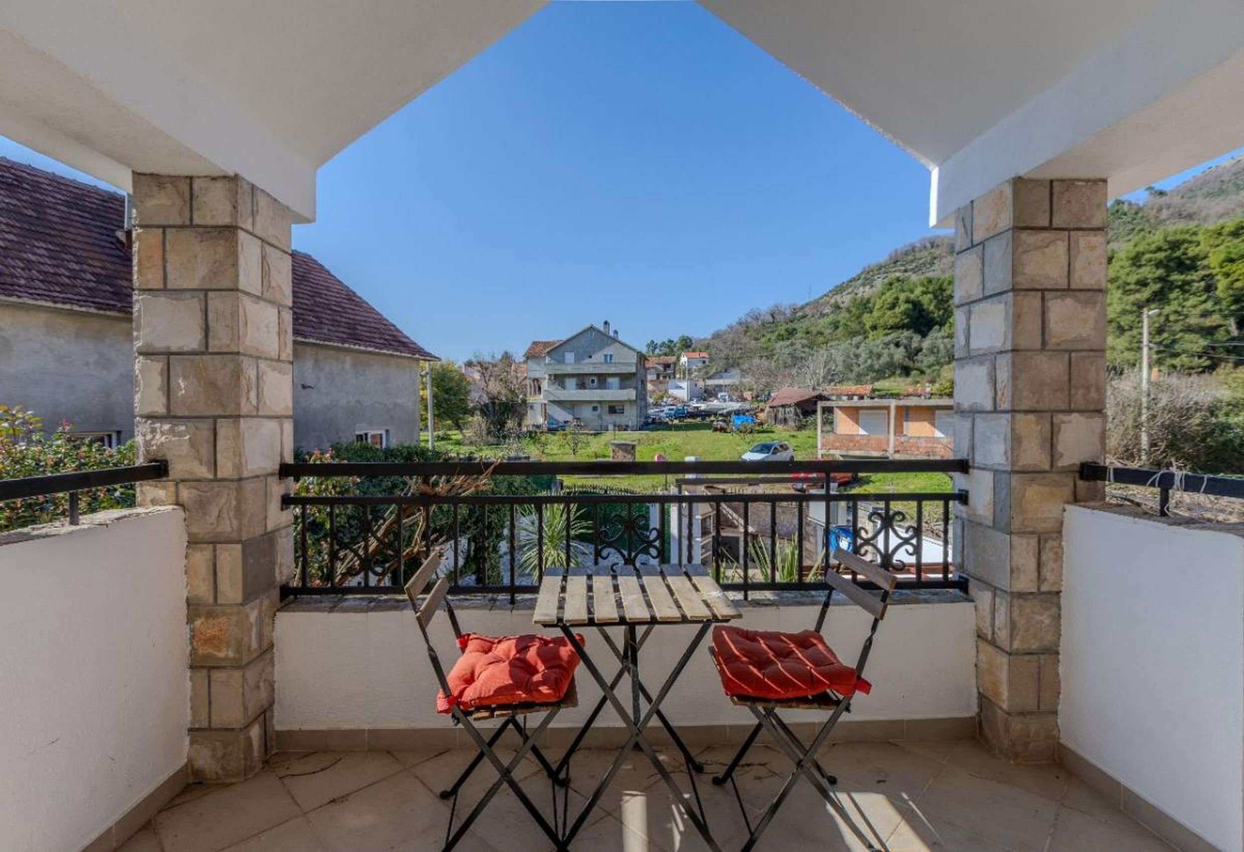 Balcon avec colonnes en pierre et vue sur les montagnes dans une maison à Tivat, Monténégro, avec une table et deux chaises.