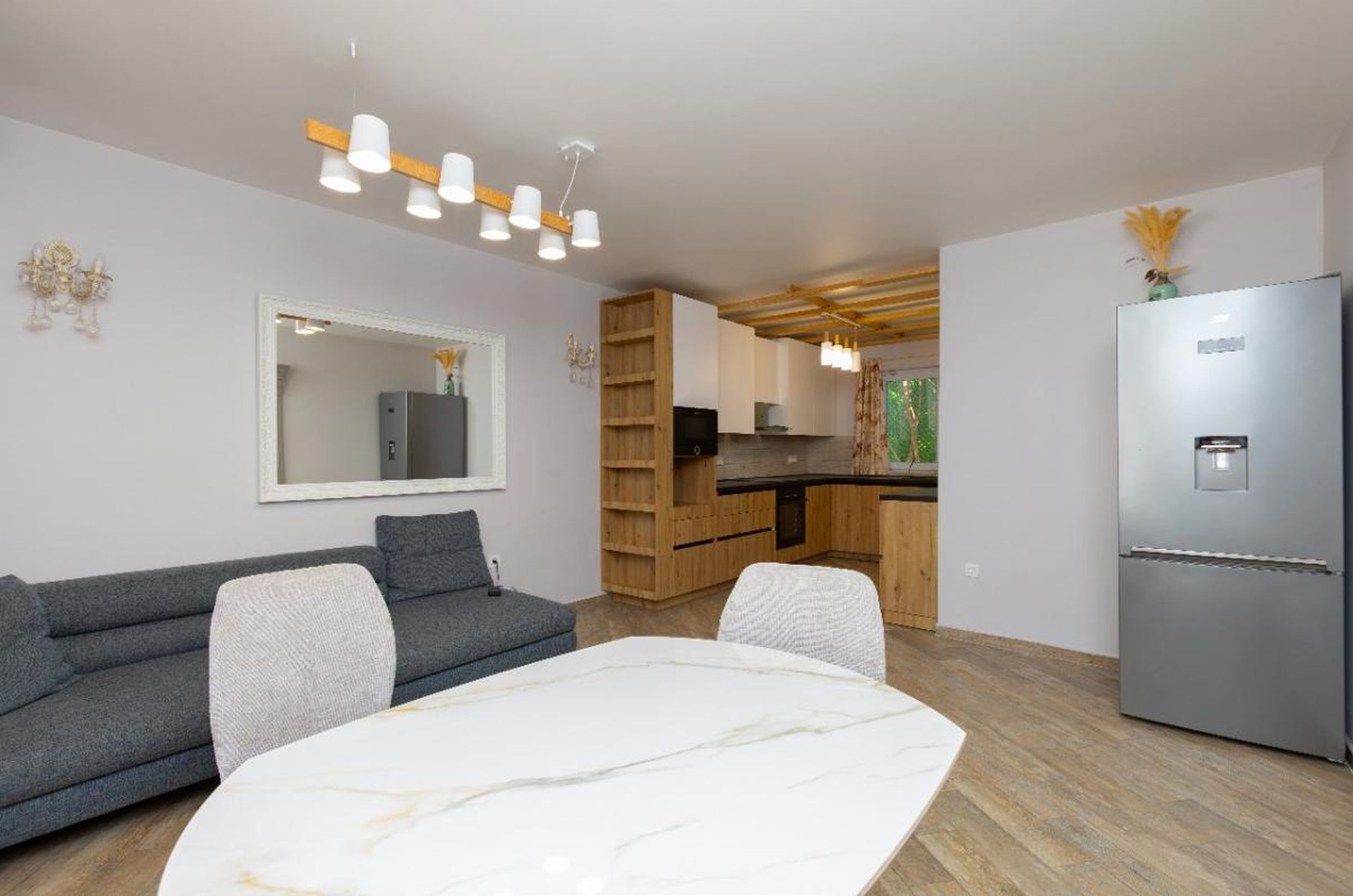 Salon moderne avec cuisine dans une maison à Tivat, Monténégro : canapé gris, table en marbre et mobilier encastré en bois.
