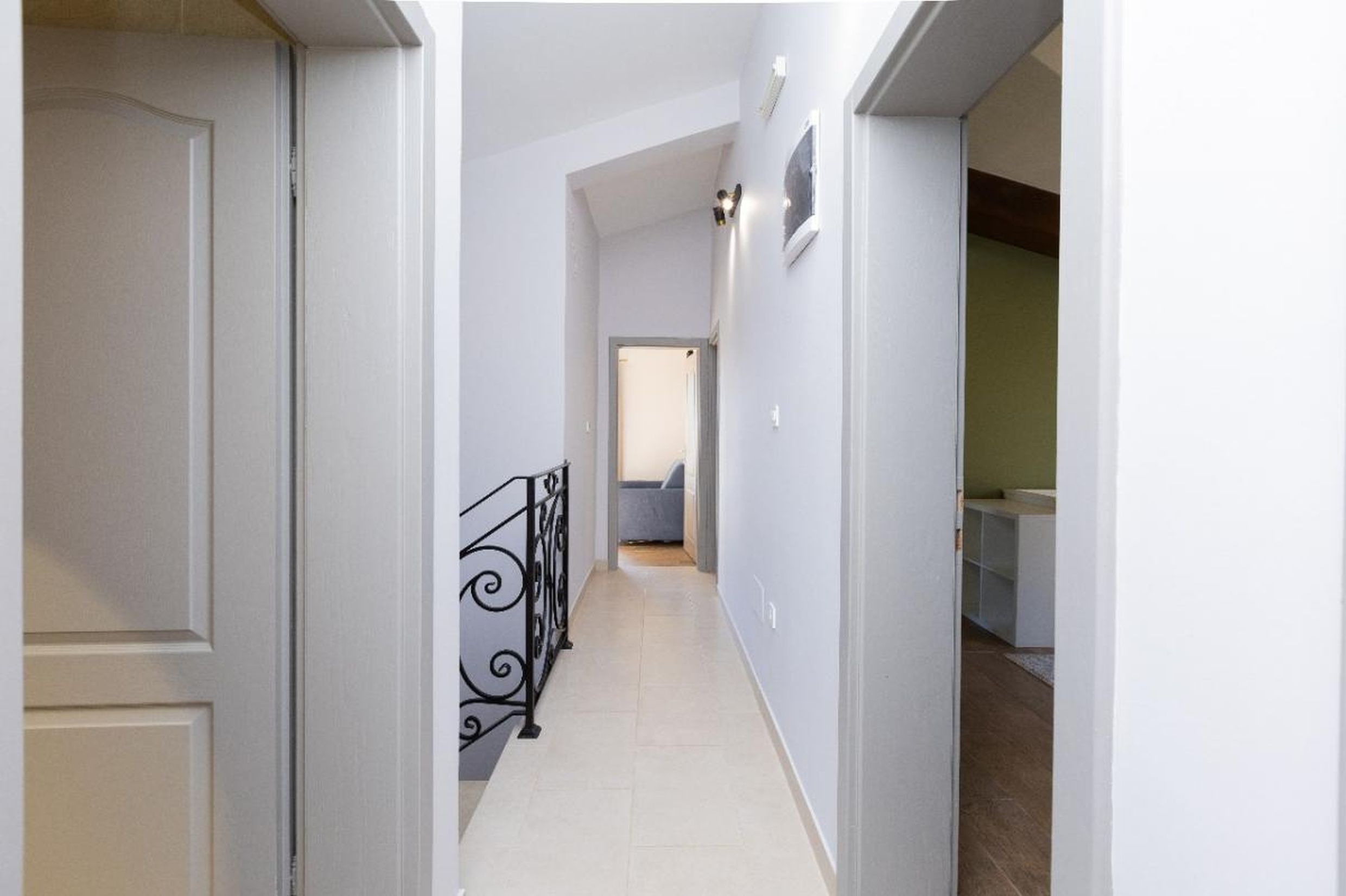 Couloir lumineux dans une maison à Tivat, Monténégro : rampe d’escalier en fer forgé, sol carrelé et portes intérieures.
